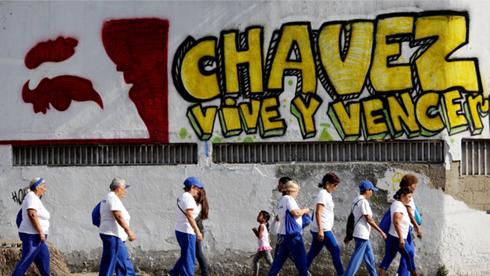 Pedestrians walks past graffiti that reads in Spanish; "Chavez lives and will prevail," outside the military hospital in Caracas, Venezuela, Tuesday, March 5, 2013. A brief statement read on national television by Communications Minister Ernesto Villegas late Monday carried the sobering news about the charismatic 58-year-old leader's deteriorating health. Villegas said President Hugo Chavez is suffering from "a new, severe infection." The state news agency identified it as respiratory. (AP Photo/Ariana Cubillos)