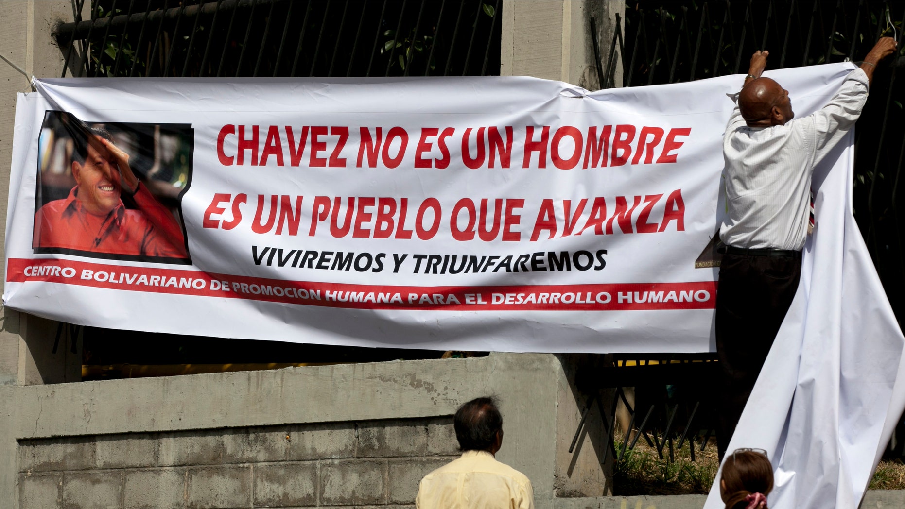 A man hangs a banner showing a picture of Venezuela's President Hugo Chavez outside the Military Hospital, where Chavez is allegedly receiving treatment, in Caracas, Venezuela, Thursday, Feb. 21, 2013. (AP Photo/Ariana Cubillos)