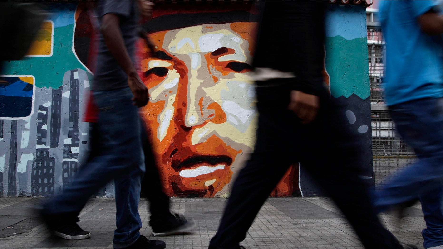 People walk by a mural of Venezuela's President Hugo Chavez in Caracas, Venezuela, Friday, April 20, 2012. Chavez is in Cuba to continue with cancer treatment. (AP Photo/Ariana Cubillos)