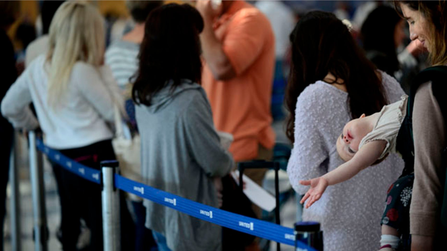 September 26, 2014: Ann Walden and her 15 month-old daughter Delphine wait in line after their flight to Baton Rouge was delayed at O'Hare International Airport in Chicago. All flights in and out of Chicago's two airports were halted Friday after a fire at a suburban air traffic control facility sent delays and cancellations rippling through the U.S. air travel network. (AP Photo/Paul Beaty)