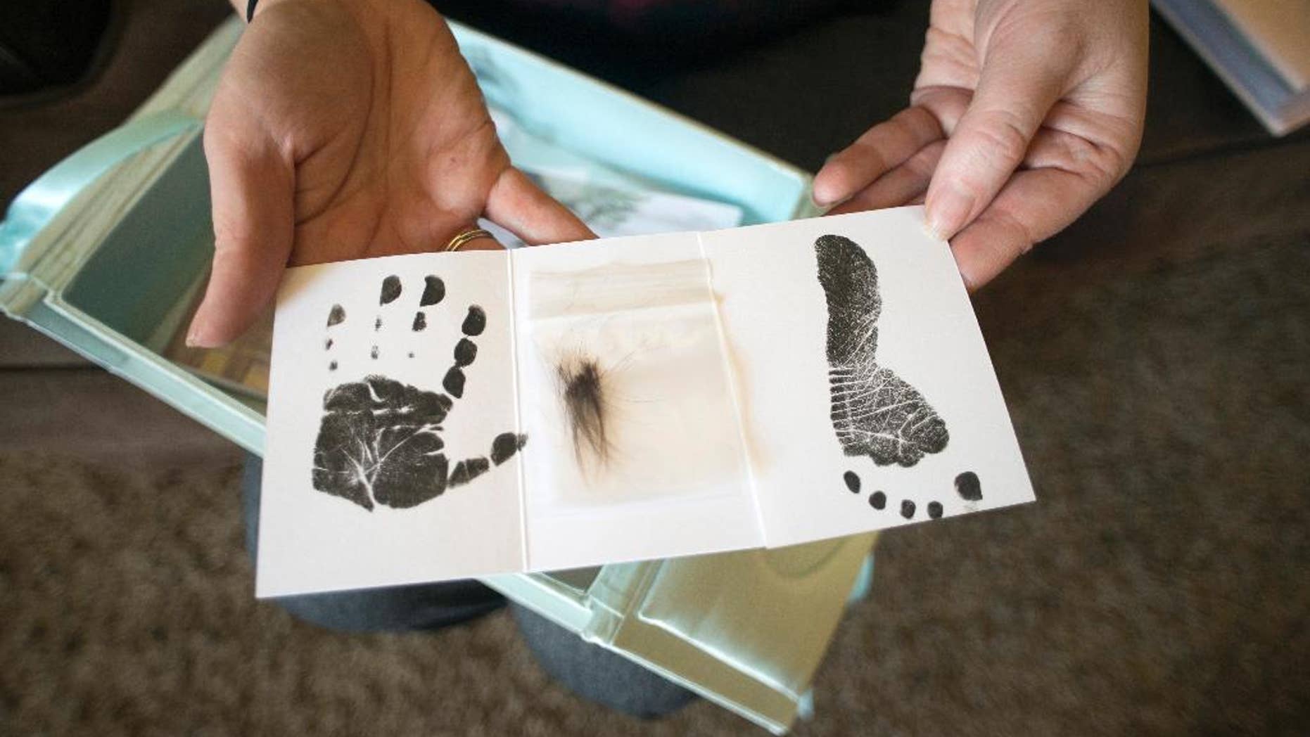 FILE - In this Nov. 13, 2014 file photo, sitting in her home in Butte, Mont., Jennifer Blaz, 34, holds the small hand print, hair clipping and footprint given to her by the hospital after the death of her daughter, Mattisyn, in 2013. Earlier in the day, Matthew Blaz, 33, was sentenced to life in prison without parole for the death of their infant daughter. In a document obtained by The Associated Press in August 2015, the federal government says it will strip Montana of a child abuse prevention grant if the state does not start providing the public with required details about children who die from abuse and neglect. The AP obtained the letter from Montana officials after filing a federal Freedom of Information Act with HHS. (AP Photo/Lido Vizzutti)