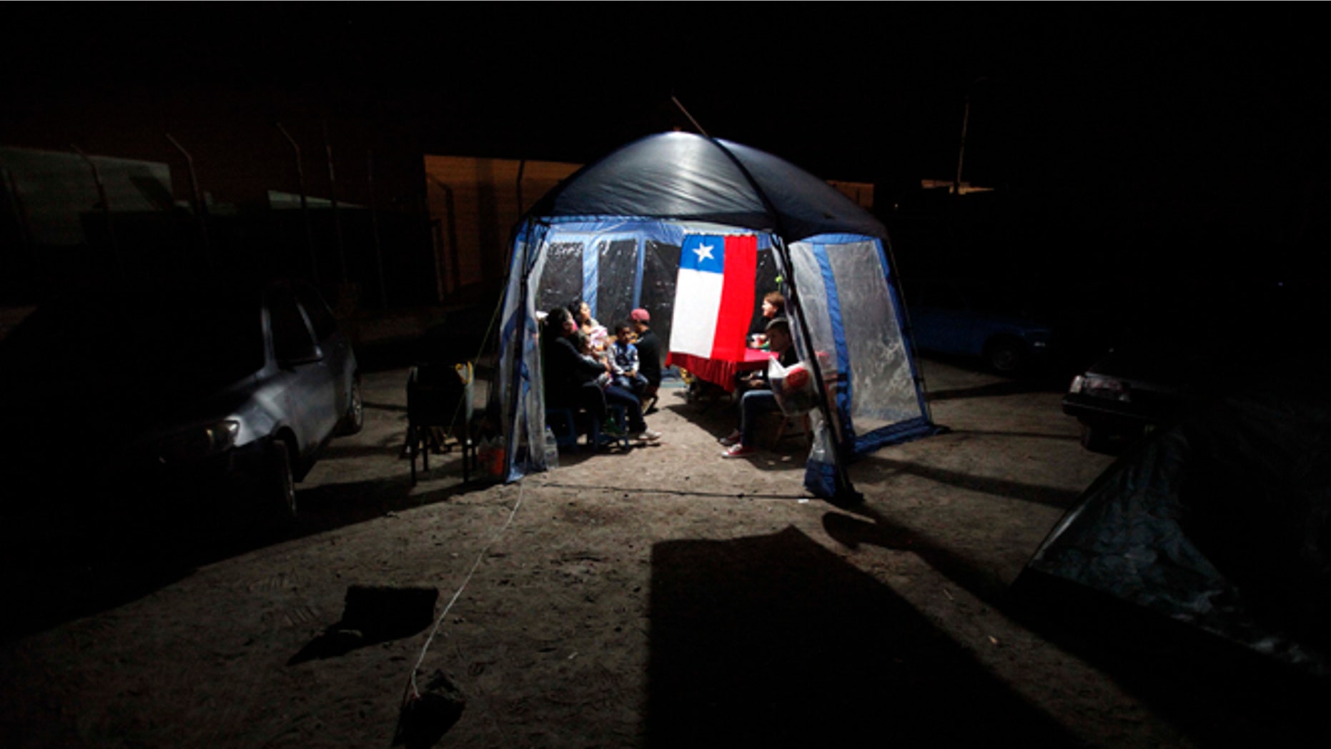 People take shelter under a tent decorated with a Chilean flag after evacuating their homes due to earthquakes in Alto Hospicio, Chile, Thursday, April 3, 2014. Coastal residents of Chile's far north spent a second sleepless night outside their homes as major aftershocks continued Thursday following a magnitude-8.2 earthquake that damaged several thousand homes and caused six deaths. (AP Photo/Luis Hidalgo)