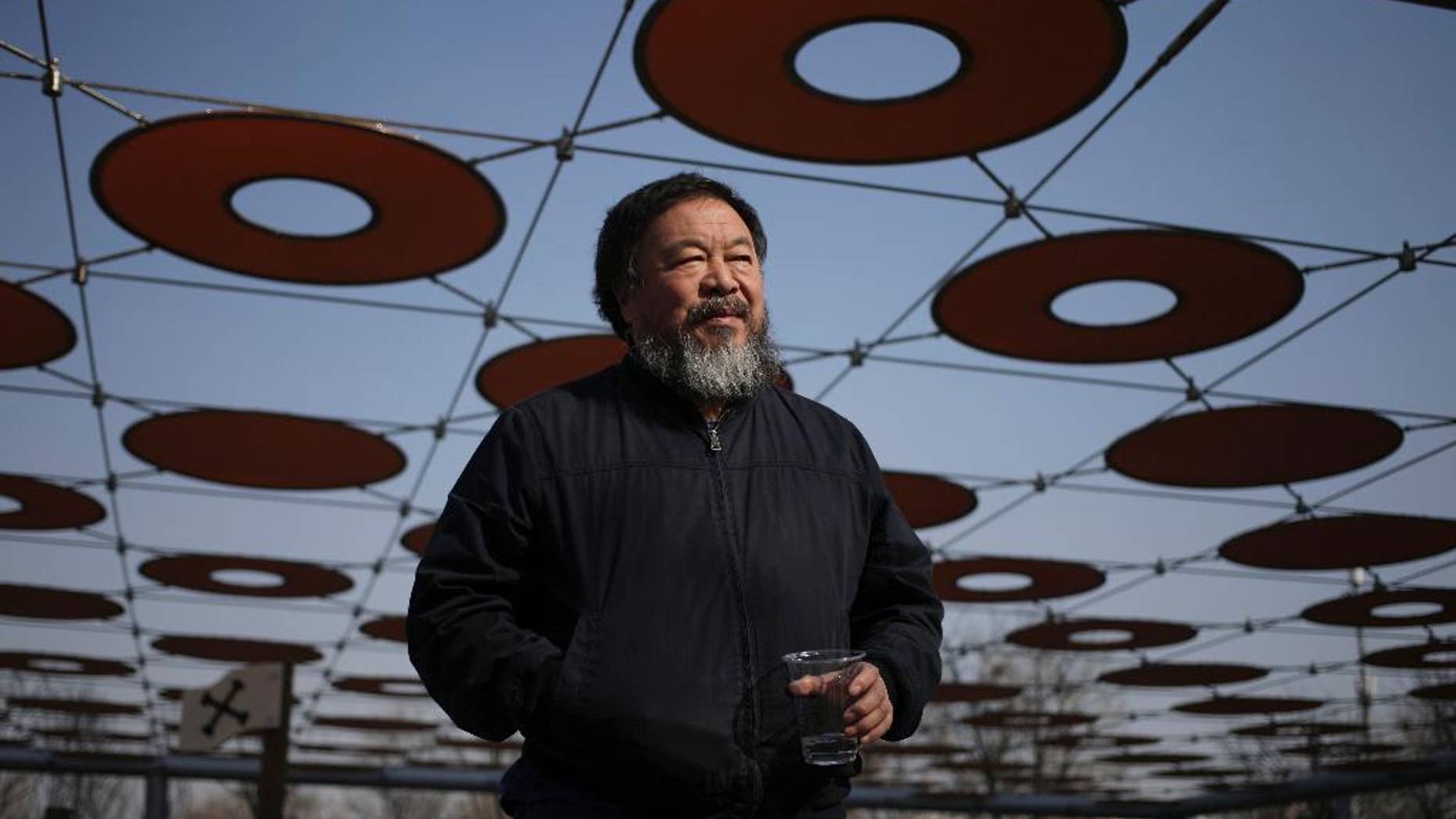 FILE - In this March 24, 2015 file photo, Chinese dissident artist Ai Weiwei walks near a playground outside a shopping mall in Beijing. Ai has his passport back four years after it was confiscated by authorities. Ai on Wednesday, July 22, 2015, posted a photo of himself on Instagram holding a Chinese passport with the caption, “Today, I got my passport.” (AP Photo/Andy Wong, File)