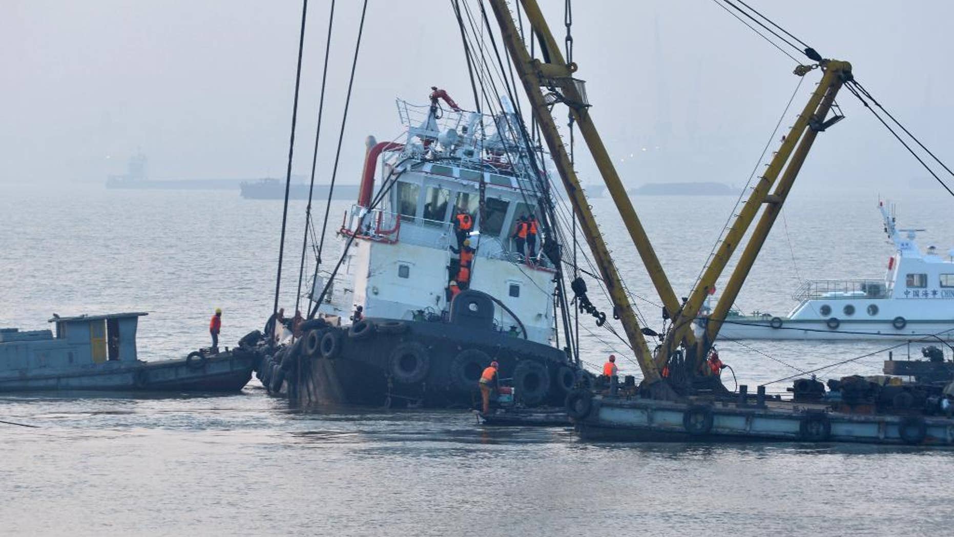 In this photo released by China's Xinhua News Agency, rescuers approach the lifted wreckage of capsized tug boat "Wanshenzhou 67" on the Yangtze River near Jingjiang, east China's Jiangsu Province, Saturday, Jan. 17, 2015. Authorities confirmed 21 people dead in the capsizing of the tugboat with an international team on a test voyage in eastern China, after rescuers dragged the overturned vessel to shallow waters and scoured it Saturday. (AP Photo/Xinhua, Shen Peng) NO SALES