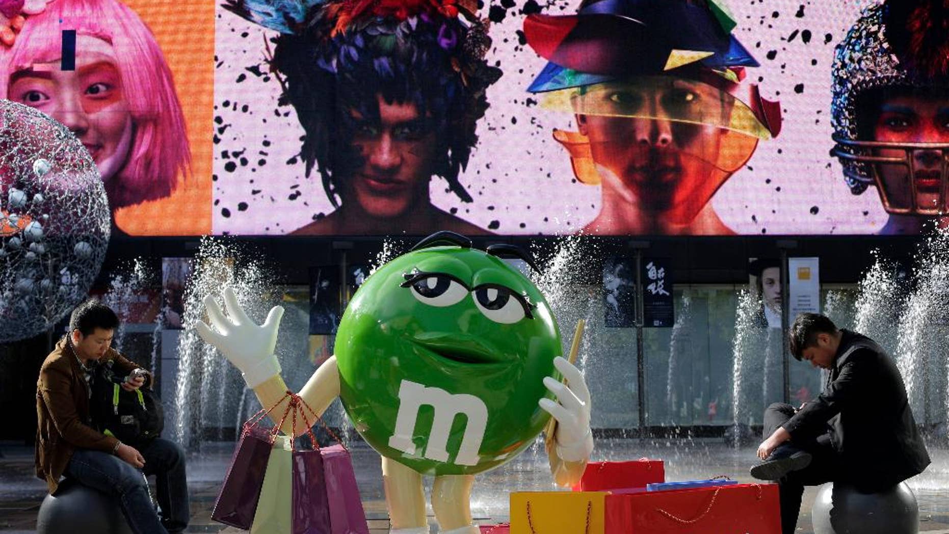 Chinese men browse their mobile phones near a M&M chocolates figure on display at a shopping mall in Beijing, Wednesday, Oct. 28, 2015. Facing pressure to pep up a cooling economy, Chinese leaders met on Monday and will announce a five-year plan effort to shift China from reliance on trade and investment to more self-sustaining growth driven by domestic consumption. The Chinese words on the bag reads "Don't worry how much you shop, just spend to release stress" (AP Photo/Andy Wong)