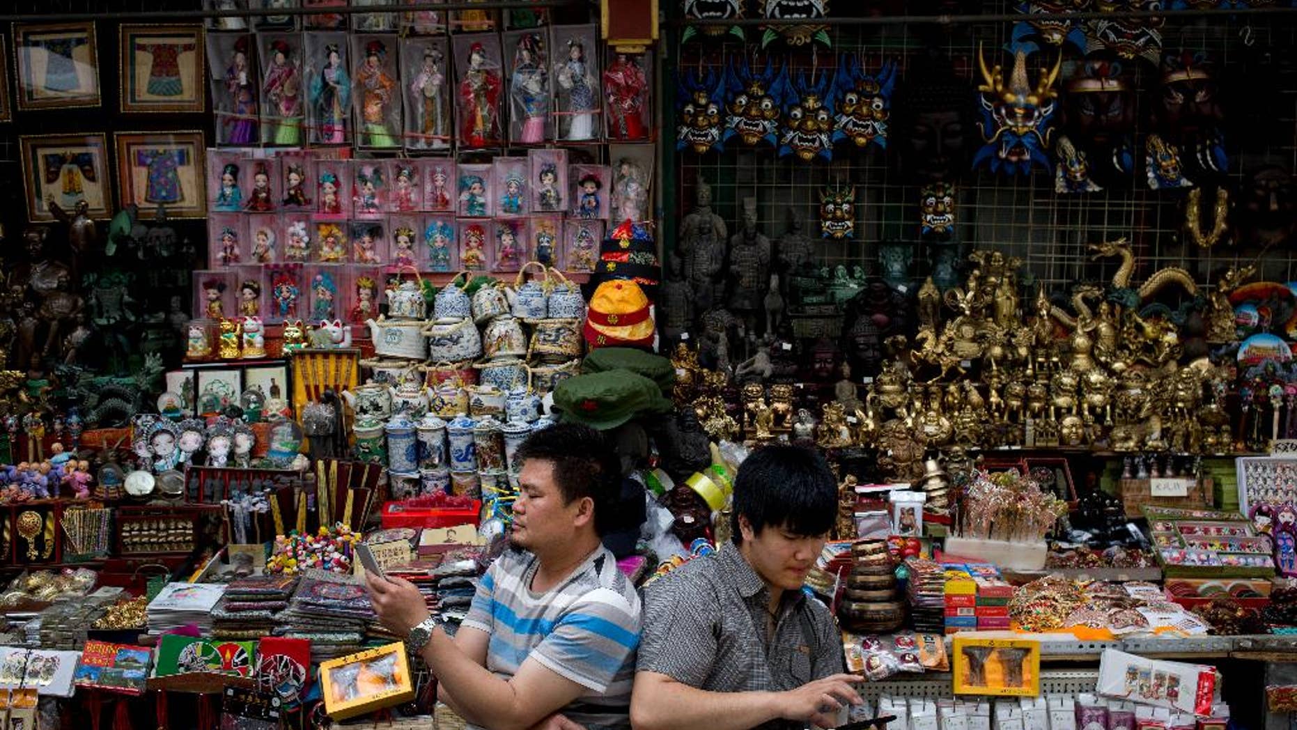 Vendors browse their smartphones as they wait for customer at their store selling Chinese made souvenirs at the Wangfujing shopping district in Beijing, China Thursday, May 21, 2015. Manufacturing in China shrank for the third straight month in May as demand remained soft, raising the chances of more stimulus to prop up growth in the world's No. 2 economy. (AP Photo/Andy Wong)