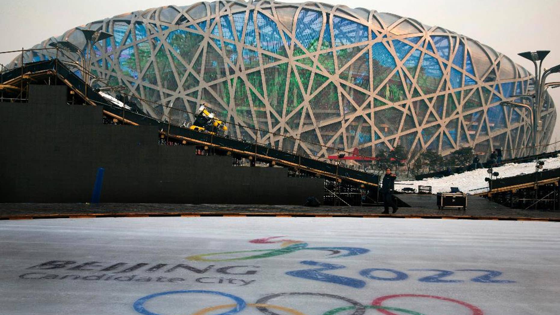 FOR STORY OLYMPICS 2022 BID - FILE - In this Dec. 26, 2014 file photo, a worker walks past an ice rink with the logo for Beijing's Winter Olympics bid ahead of a countdown event to the new year in front of the iconic Beijing National Stadium "Bird's Nest" in Beijing. The International Olympic Committee will be faced with two starkly different choices, Beijing and Almaty, Kazakhstan , when it selects the host city for the 2022 Winter Games, on July 31 in Kuala Lumpur, Malaysia. (AP Photo/Ng Han Guan, File)