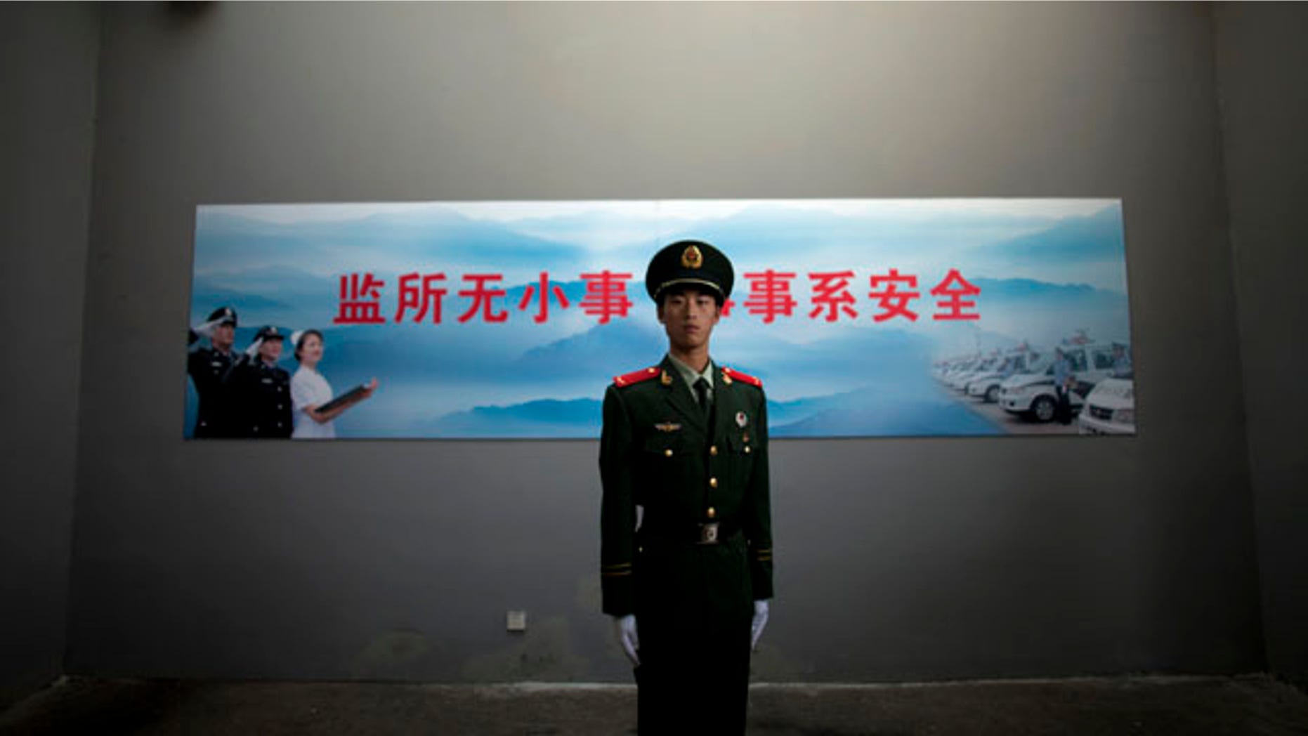 FILE - In this Oct. 25, 2012 file photo, a Chinese paramilitary policeman stands guard underneath a surveillance camera at an entrance to the Number Two Detention Center in Beijing, China. The slogan on the wall reads 'No small matter in detention center, everything concerns safety.' (AP Photo/Alexander F. Yuan, File)