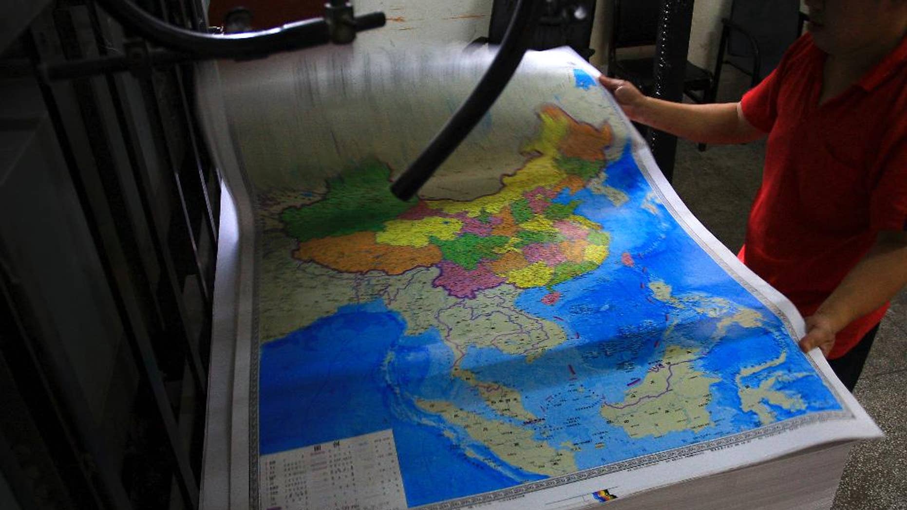 In this June 27, 2014 photo, a printing worker holds a new officially approved map of China that includes the islands and maritime area that Beijing claims in the South China Sea, at a factory in Changsha in south China's Hunan province. China has again rejected an attempt by the Philippines to challenge its territorial claims over the South China Sea through international arbitration, releasing a lengthy paper a week before the Dec. 15, 2014 deadline for China to respond to the case. China prefers to settle its disputes with discussions with the countries directly involved. But the Philippines has filed a case with an international tribunal.(AP Photo) CHINA OUT