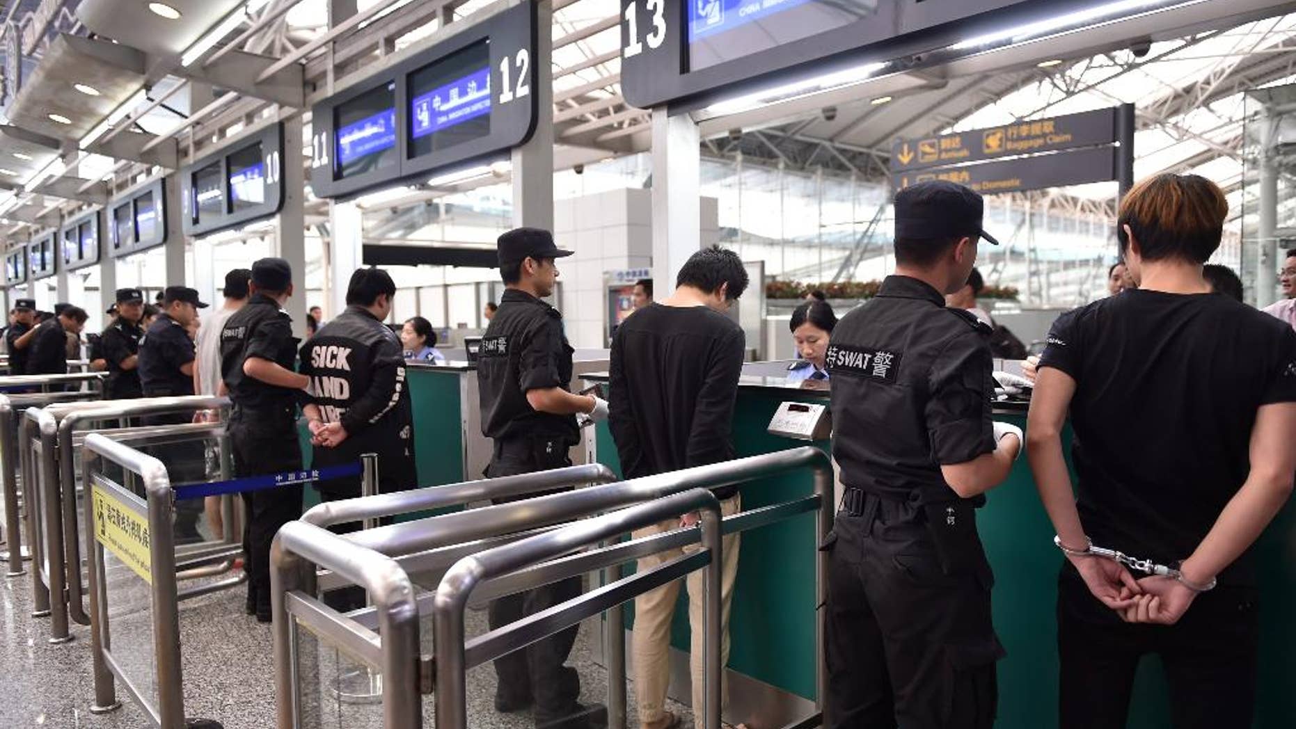 In this photo released by China's Xinhua News Agency, suspects are escorted to go through Customs by police officers at Guangzhou Baiyun International Airport in Guangzhou, capital of south China's Guangdong Province, Tuesday, Nov. 10, 2015. Over 200 Chinese citizens arrested in Cambodia and Indonesia for running telephone scams targeting Chinese victims were repatriated Tuesday to face charges in China, the Public Security Ministry said. A statement on the ministry's website said the suspects were flown back to Beijing and three other Chinese cities aboard chartered flights. They are suspected of committing upward of 4,000 major cases of cross-border telephone fraud targeting victims in more than 20 cities and provinces, the ministry said. (Liang Xu/Xinhua via AP) NO SALES
