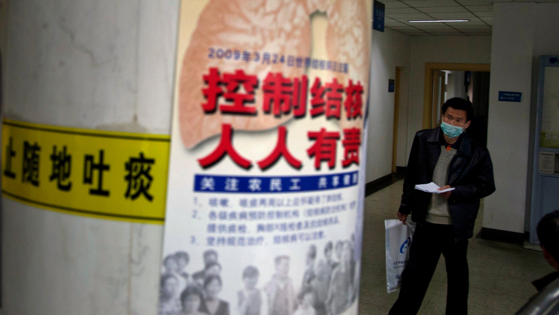 A visitor wearing a mask walks near a poster promoting tuberculosis awareness which reads "Control TB, Everyone's Duty" and a yellow "Do Not Spit" sign at the Beijing Chest Hospital. (AP Photo/Ng Han Guan)