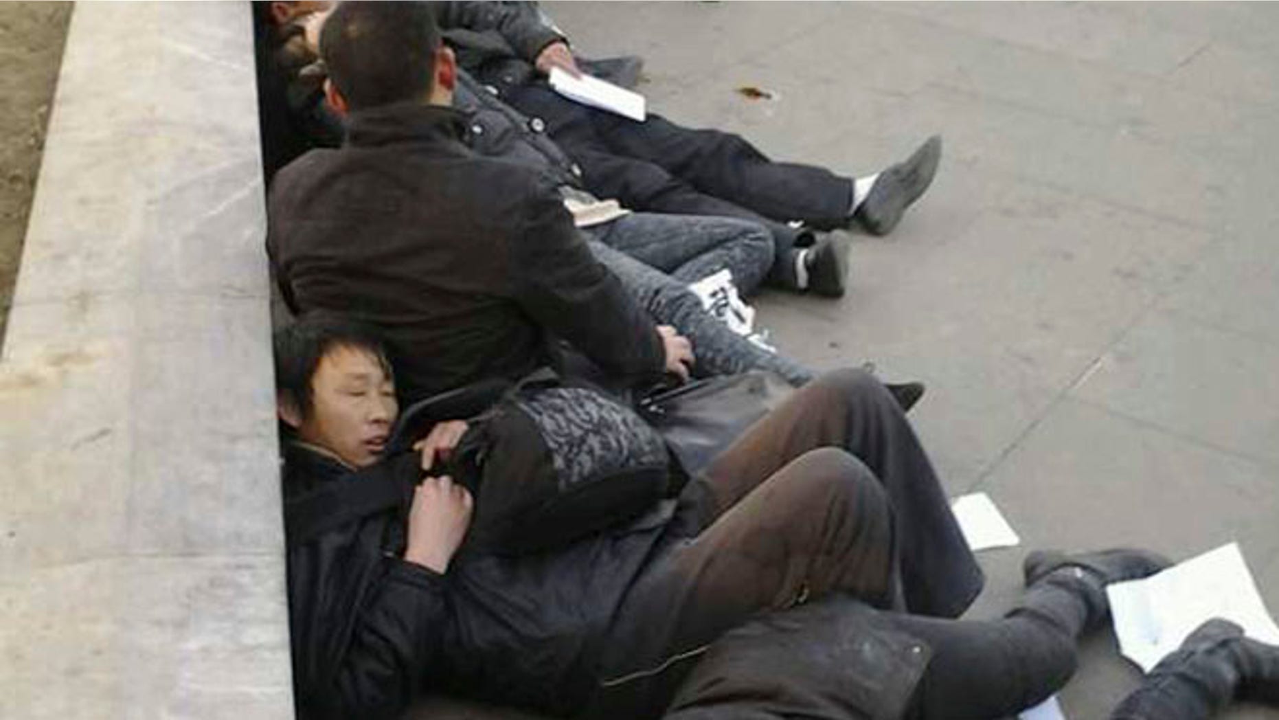 In this photo taken Dec. 10, 2013, which The Associated Press obtained on Wednesday, Dec. 11, 2013, from a friend of the petitioners, Chinese residents from Wuhan province lie on the ground after drinking pesticide near a historic watchtower in the heart of Beijing, China. A dozen central Chinese city residents protesting the demolition of their homes drank pesticide in Beijing in a desperate bid for attention that underscores the failures of a decades-old petitioning system. The photo has been authenticated based on its contents and other AP reporting.