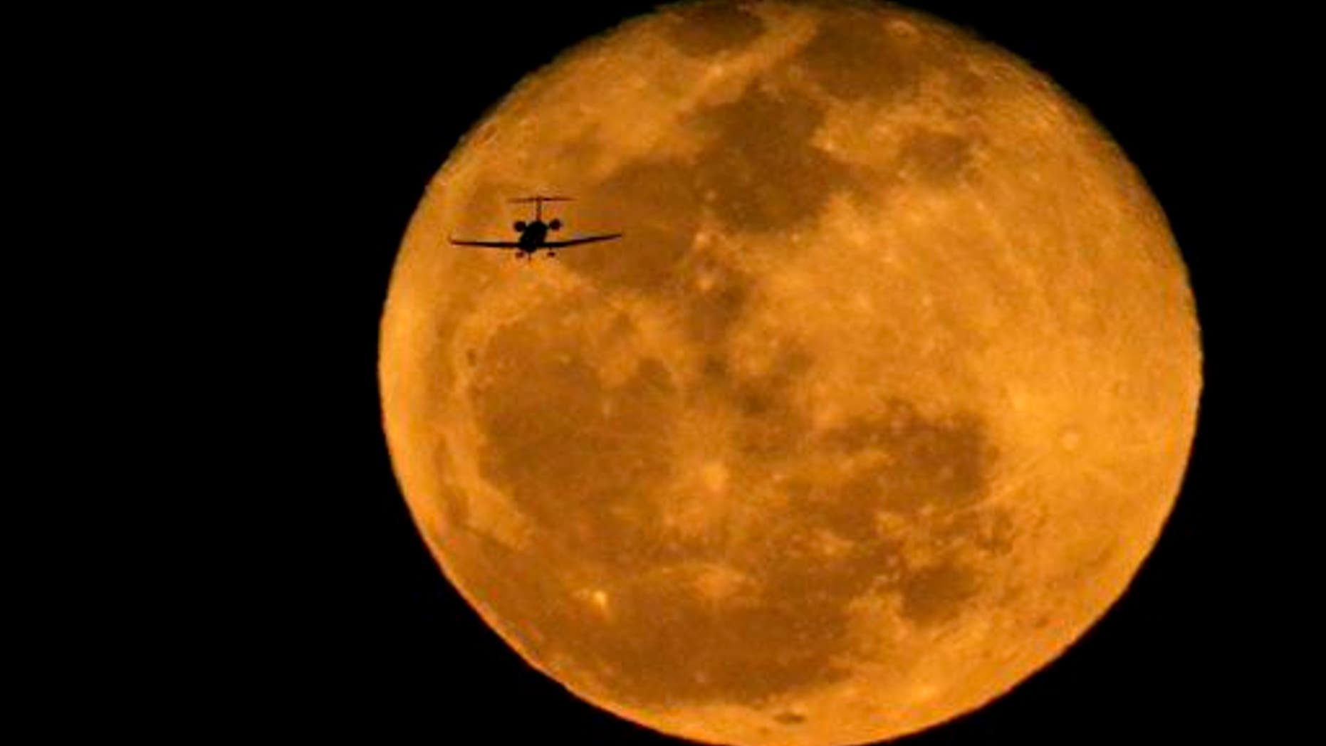 A jet is silhouetted by the rising waning moon on a landing approach at Phoenix's Sky Harbor International Airport on March 6, 2015.