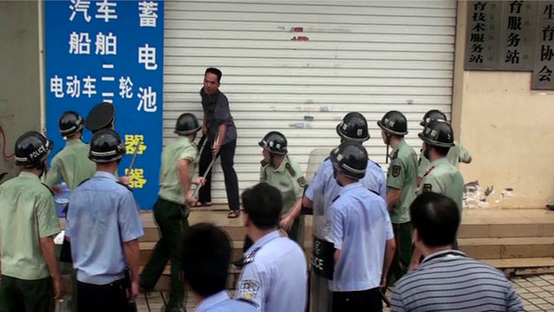 In this July 23, 2013 photo, Chinese security personnel try to subdue a knife-wielding man outside the family planning office in Dongxing city in southwest China's Guangxi province. Local media report that the man attacked the local family planning office killing two officials and injuring another four after being refused a residency permit for his fourth child that he fathered in violation of China's one-child policy. (AP Photo) CHINA OUT