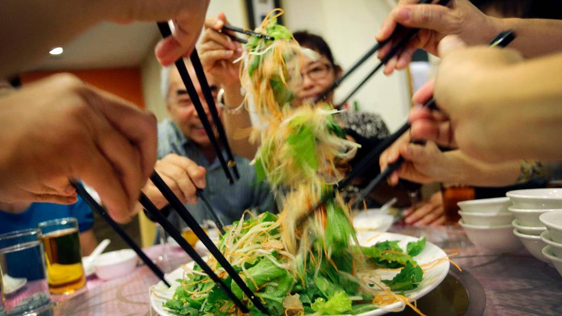 In this photo taken on Monday, Feb. 16, 2015, Cheong Lan Yang, 68, rear left, tosses "yu sheng," a raw fish salad, with family members during a family reunion dinner for Chinese New Year, at a restaurant in Singapore. This Singaporean tradition is known as “lo hei,” which means “tossing up good fortune” in Cantonese and is done at the start of family reunion dinners before Chinese New Year. The raw fish in the salad symbolizes the abundance of wealth and long life that Cheong, who lives in Australia, hopes for in the new year. “I hope this Chinese New Year brings good health because I would like to live long enough to see my grandchildren one day,” he said. “Chinese New Year is a time for family gathering and that means a lot to me because I currently live abroad, and this is a time for us to share old memories as well as make new ones.” (AP Photo/Wong Maye-E)
