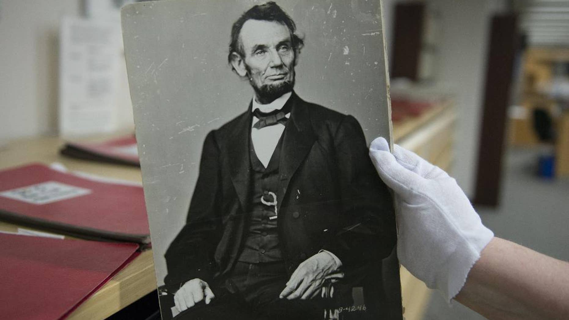 In this Monday, April 6, 2015 photo, Karen Needles holds up a photograph of President Abraham Lincoln at the National Archives in College Park, Md. Three blocks away, 150 years earlier, Lincoln was felled by an assassin's bullet. (AP Photo/Molly Riley)