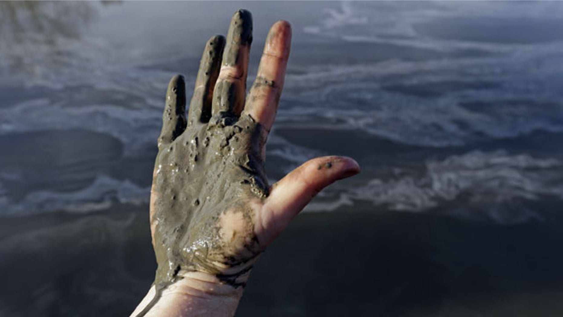 February 5, 2014: Amy Adams, North Carolina campaign coordinator with Appalachian Voices, shows her hand covered with wet coal ash from the Dan River swirling in the background as state and federal environmental officials continued their investigations of a spill of coal ash into the river in Danville, Va. Duke Energy estimates that up to 82,000 tons of ash has been released from a break in a 48-inch storm water pipe at the Dan River Power Plant in Eden N.C. on Sunday. (AP Photo/Gerry Broome)