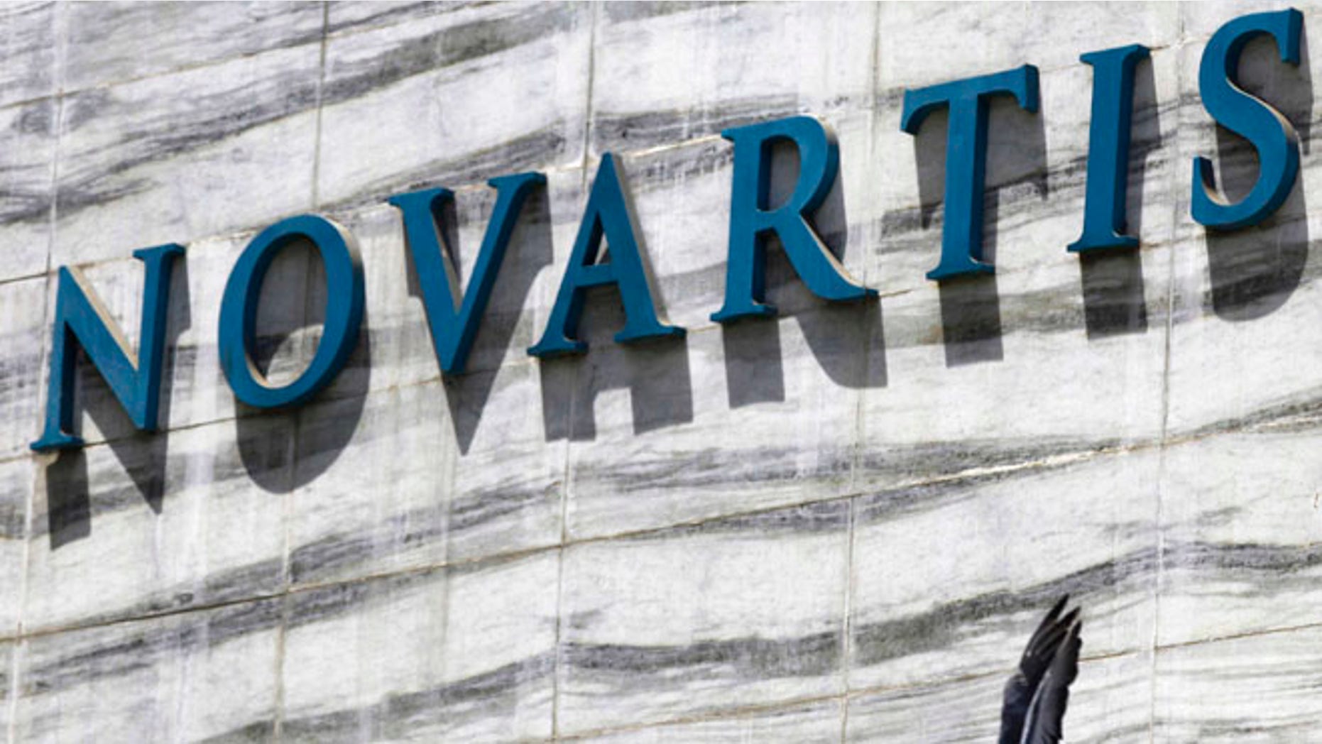 FILE - In this April 1, 2013 file photo, a dove flies near the logo of Novartis India Limited at their head office in Mumbai, India. Colombiaâs government announced on Tuesday, May 17, 2106, that it is giving pharmaceutical giant Novartis a few weeks to lower prices on a popular cancer drug or see its monopoly on production of the medicine broken and competition thrown open to generic rivals. (AP Photo/Rafiq Maqbool, File)