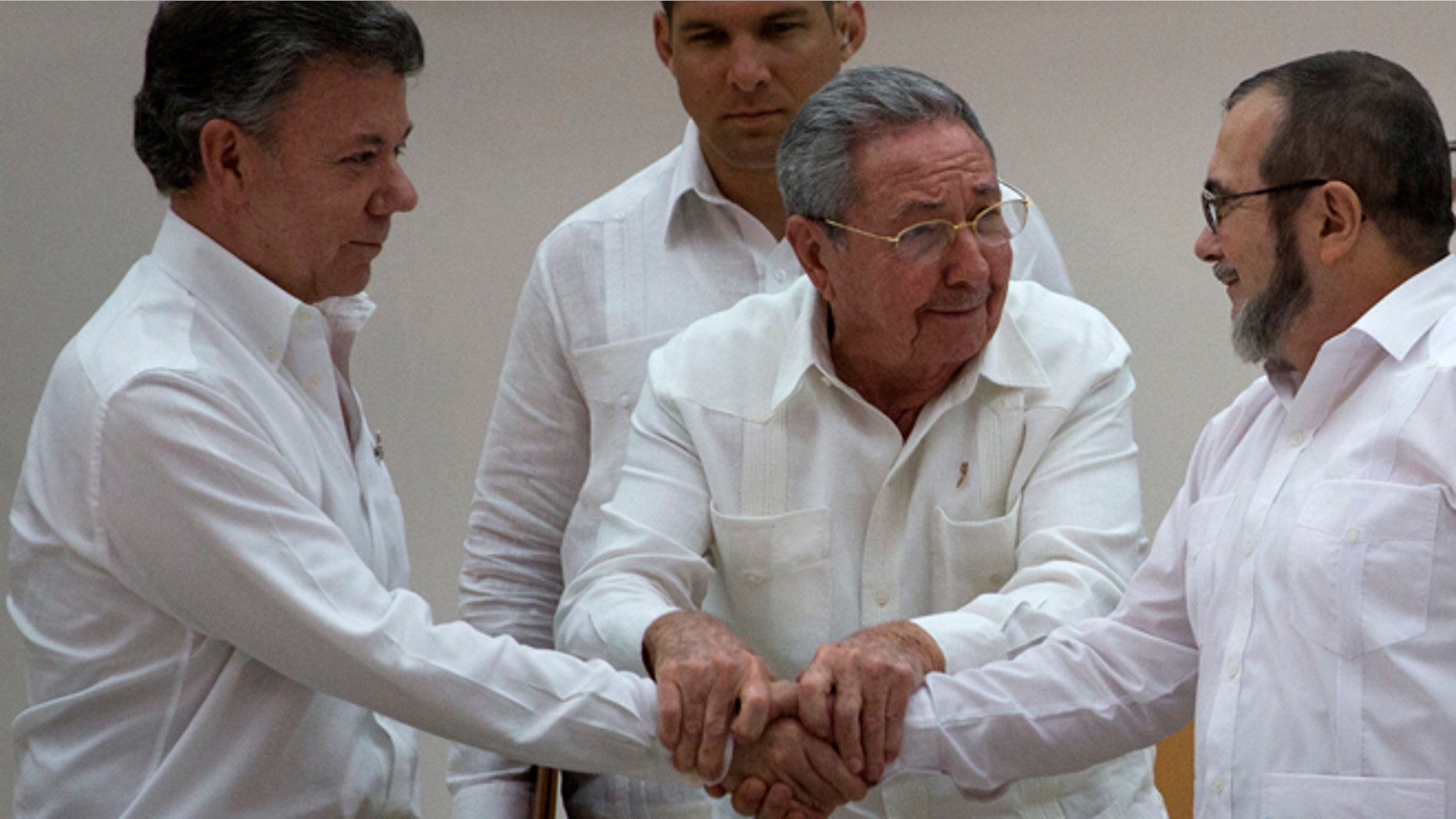 Cuba's President Raul Castro, center, encourages Colombian President Juan Manuel Santos, left, and Commander the Revolutionary Armed Forces of Colombia or FARC, Timoleon Jimenez to shake hands, in Havana, Cuba, Wednesday, Sept. 23, 2015. In a joint statement, Santos and the FARC said they have overcome the last significant obstacle to a peace deal by settling on a formula to compensate victims and punish belligerents for human rights abuses. (AP Photo/Desmond Boylan)