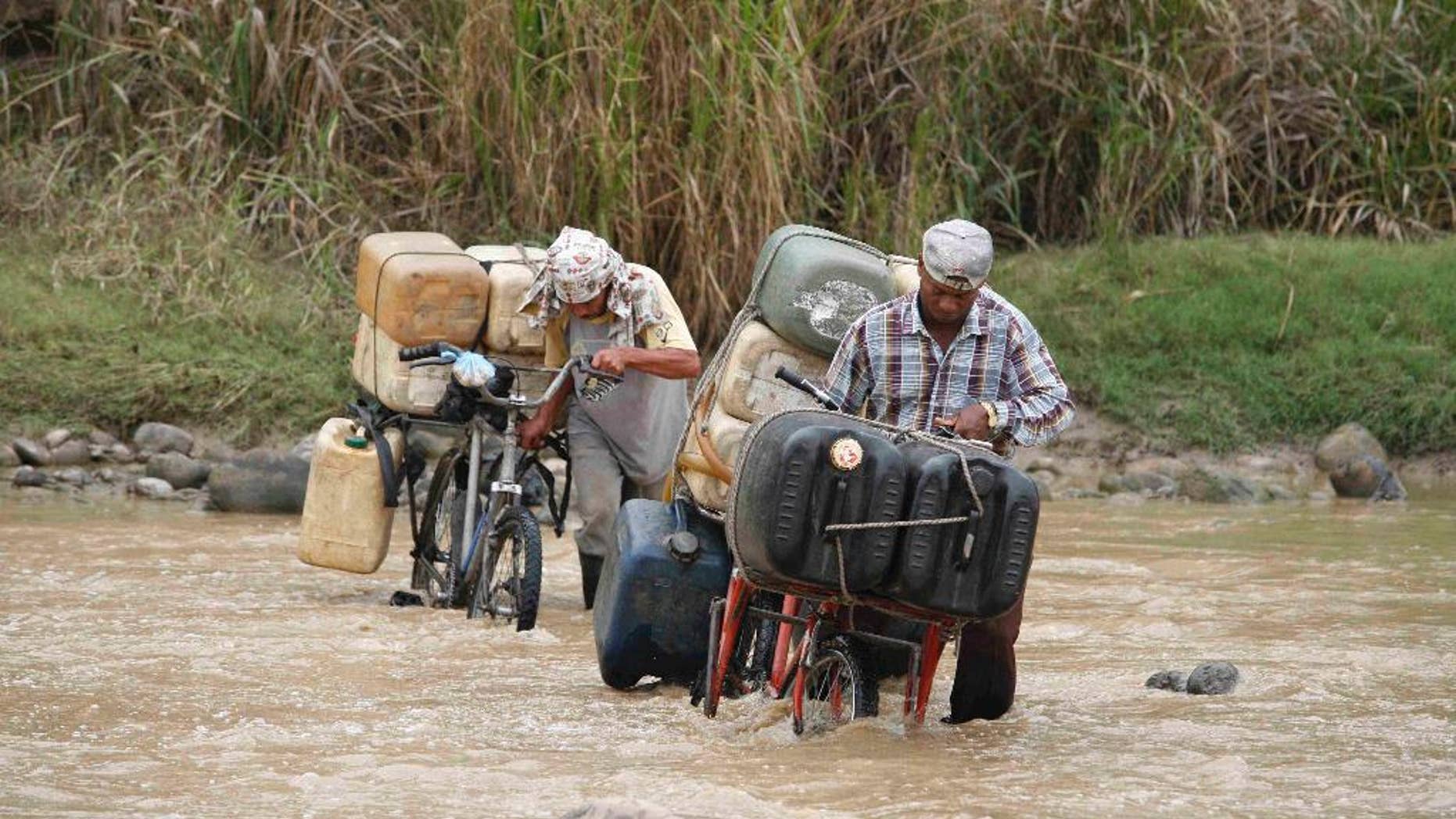 FILE - In this March 7, 2008 file photo, smugglers cross the Tachira River carrying Venezuela gasoline into Colombia, in Cucuta, at the Colombian border with Venezuela. President Nicolas Maduro has ordered the closure of a major border crossing with Colombia after three soldiers were attacked while looking for smugglers. Maduro late Wednesday, Aug. 19, 2015, said the normally busy border in western Tachira state would remain closed for 72 hours. (AP Photo/William Fernando Martinez, File)