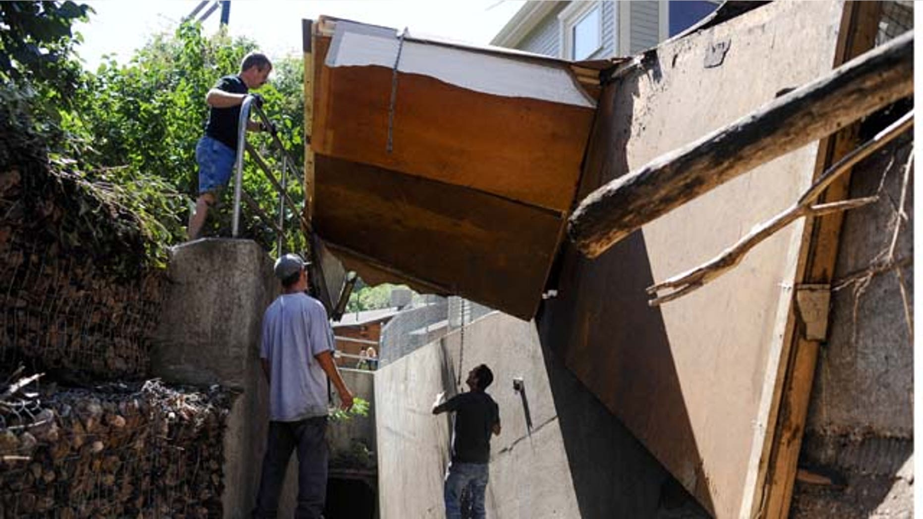 August 10, 2013: From left, Dan McCormack, Chris Lambrite Jr., and Chris Lambrite work to remove three sides of a cottage from a drainage after the entire building was ripped off its foundation by a flash flood that hit Manitou Springs, Colo.