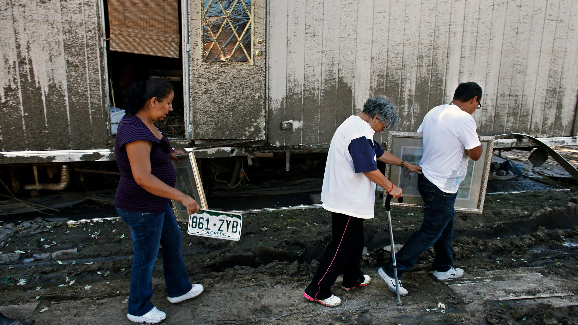 In this Sept. 24, 2013, photo, resident Mari Partida, left, walks with the plate from her destroyed car, as her neighbor Sofia Mendez leans on her son for support as he carries a painting recovered from their trailer, one of the many homes now declared uninhabitable due to permanent flood damage at a trailer park in Evans, Colo. Many undocumented immigrants working in the U.S. have returned to their mobile home parks in flood-ravaged Colorado to find that there was little left to salvage. Like many in the stricken region, they didnt have flood insurance. And because many are not citizens or legal residents, they cant get government help. (AP Photo/Brennan Linsley)