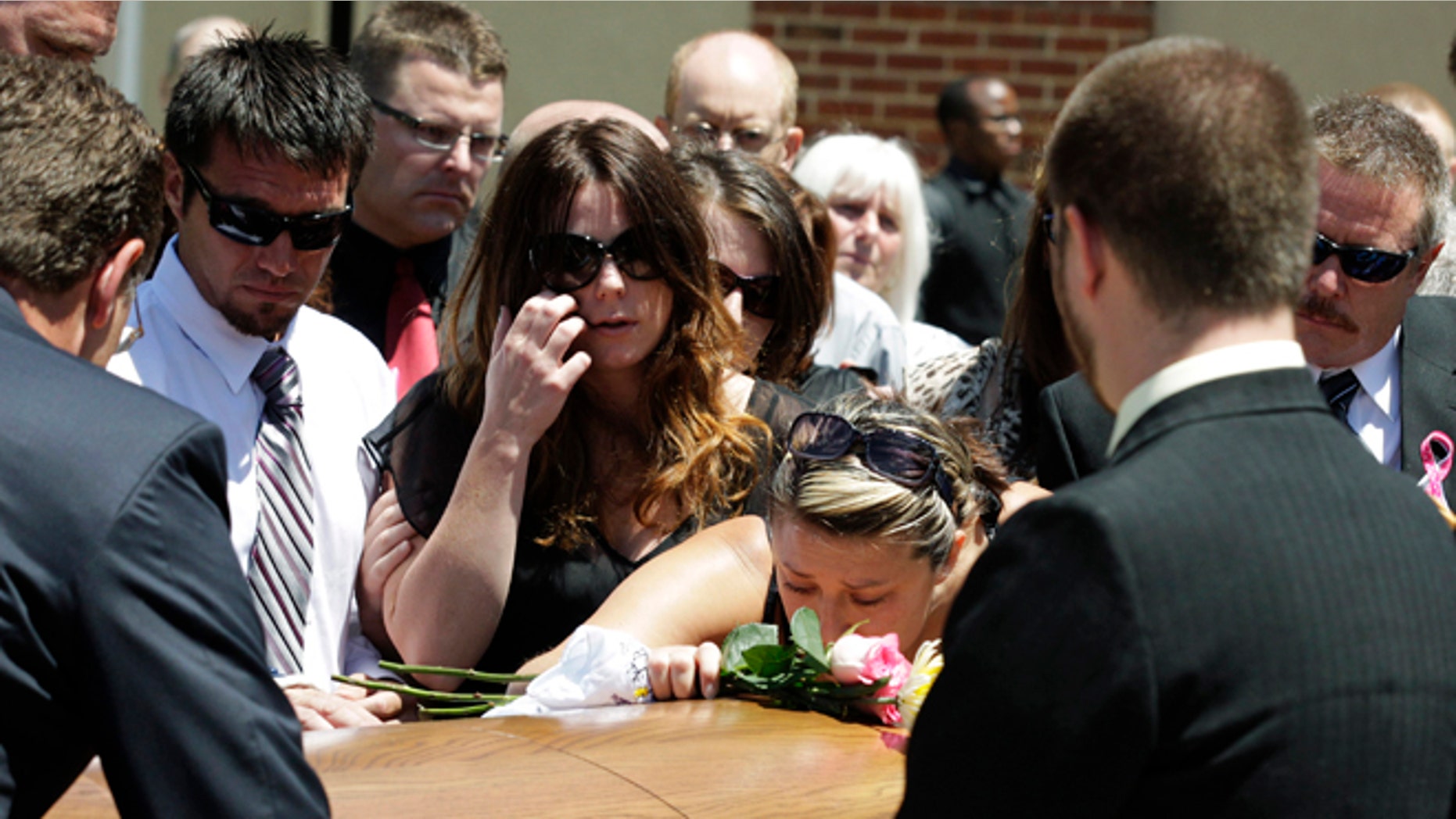 July 26, 2012: Amanda Medek, center left, looks on as her cousin Amber Vigil, center right, kisses the casket of Amanda's sister Micayla Medek, following Micayla's funeral in Denver.
