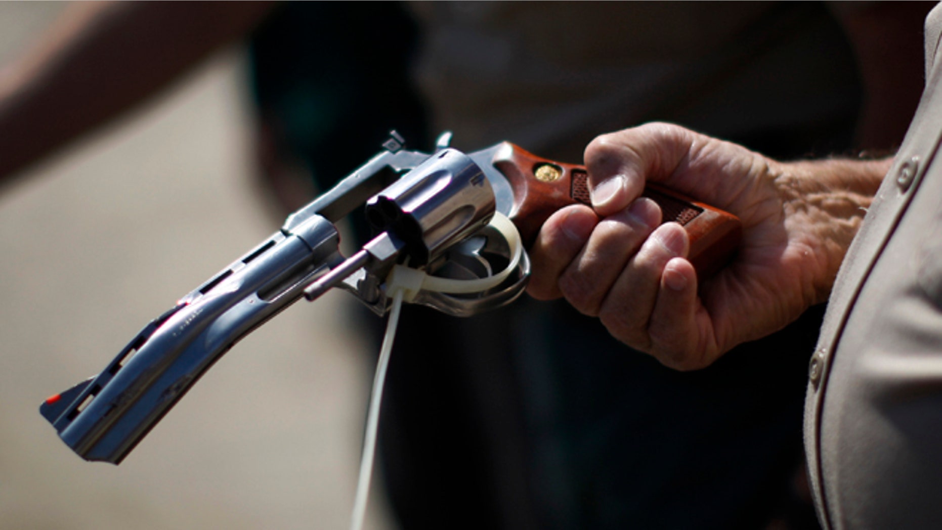 FILE: July 30, 2013: A deputy sheriff looks at a disabled gun to be melted down at a gun buy-back program in Los Angeles, Calif.
