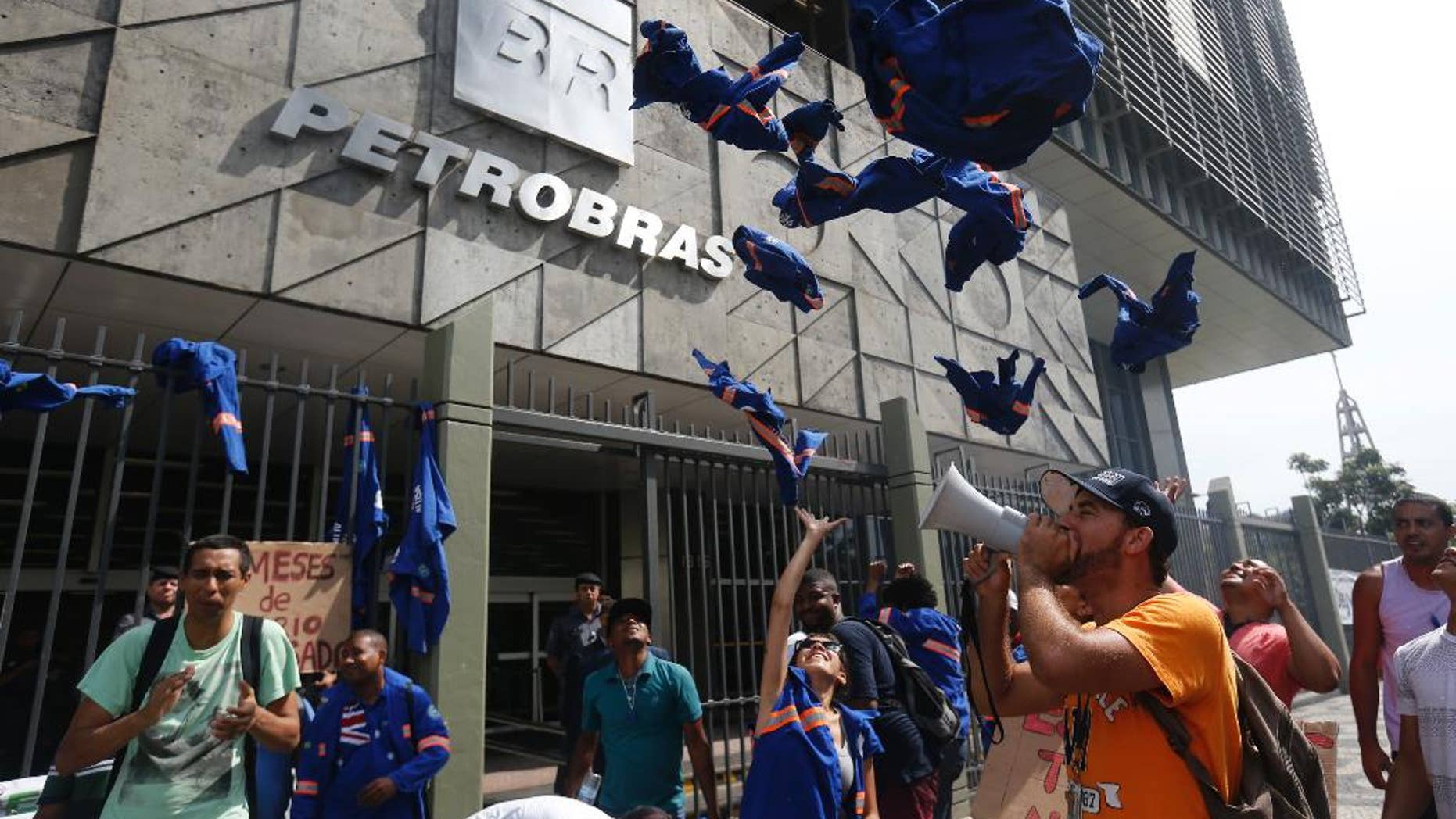 FILE - In this Feb. 4, 2015 file photo, workers whose company is contracted by Brazil's government-run oil company Petrobras throw their work uniforms at Petrobras headquarters to protest corruption, in Rio de Janeiro, Brazil. Petrobras was accused by federal prosecutors of the biggest corruption scheme in Brazil’s history in 2014, in allegations that at least $2 billion in bribes were paid out over about a decade. Several top officers resigned and even pulled leading politicians into ongoing investigations. (AP Photo/Silvia Izquierdo, File)