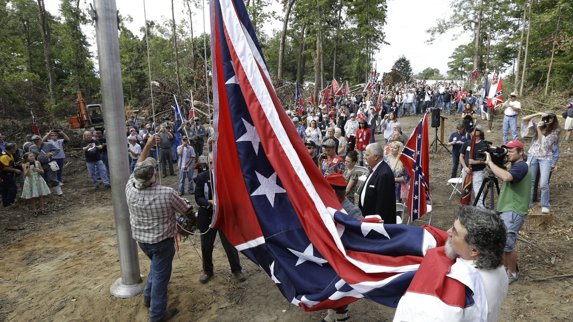 A group called "Virginia Flaggers" raise the Confederate battle flag on a pole near Interstate 95 in Chester, Va., Saturday, Sept. 28, 2013. Hundreds gathered Saturday in freshly cleared woods along Interstate 95 to celebrate the raising of a Confederate battle flag, an event that stirred strong feelings among those who view it as a symbol of division. (AP Photo/Steve Helber)