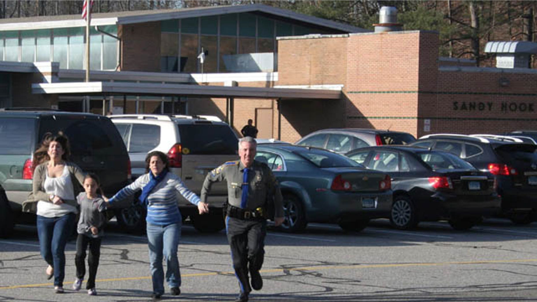 FILE - In this Friday, Dec. 14, 2012, file photo provided by the Newtown Bee, a police officer leads two women and a child from Sandy Hook Elementary School in Newtown, Conn. (AP Photo/Newtown Bee)