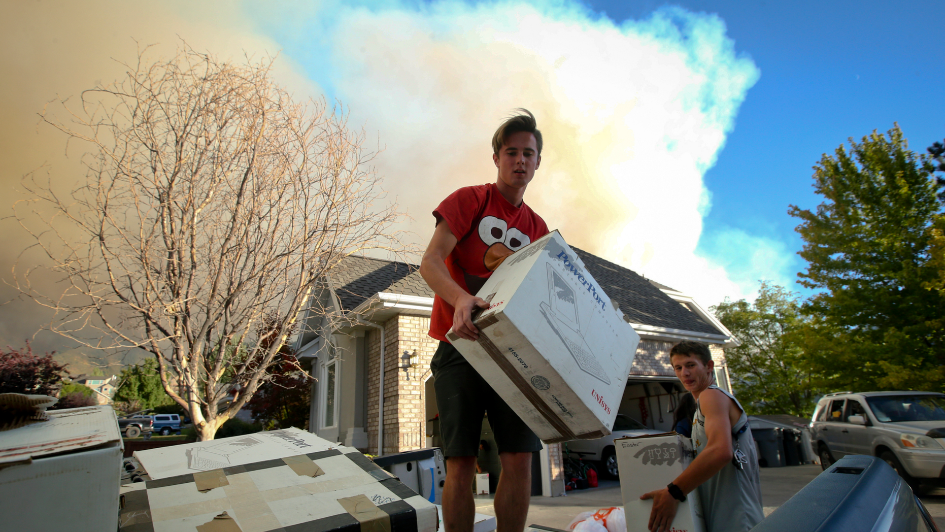 In this Thursday, Sept. 13, 2018, photo Brandon Morgan, 17, center, loads items into a truck as his friend, Carter Wilkey, 16, helps Morgan evacuate from his Elk Ridge, Utah home during a mandatory evacuation. A fast-moving Utah wildfire fanned by high-winds has more than doubled in size as it burns through dry terrain and forces evacuations of hundreds of homes, the U.S. Forest Service said Friday. (Isaac Hale/The Daily Herald via AP)
