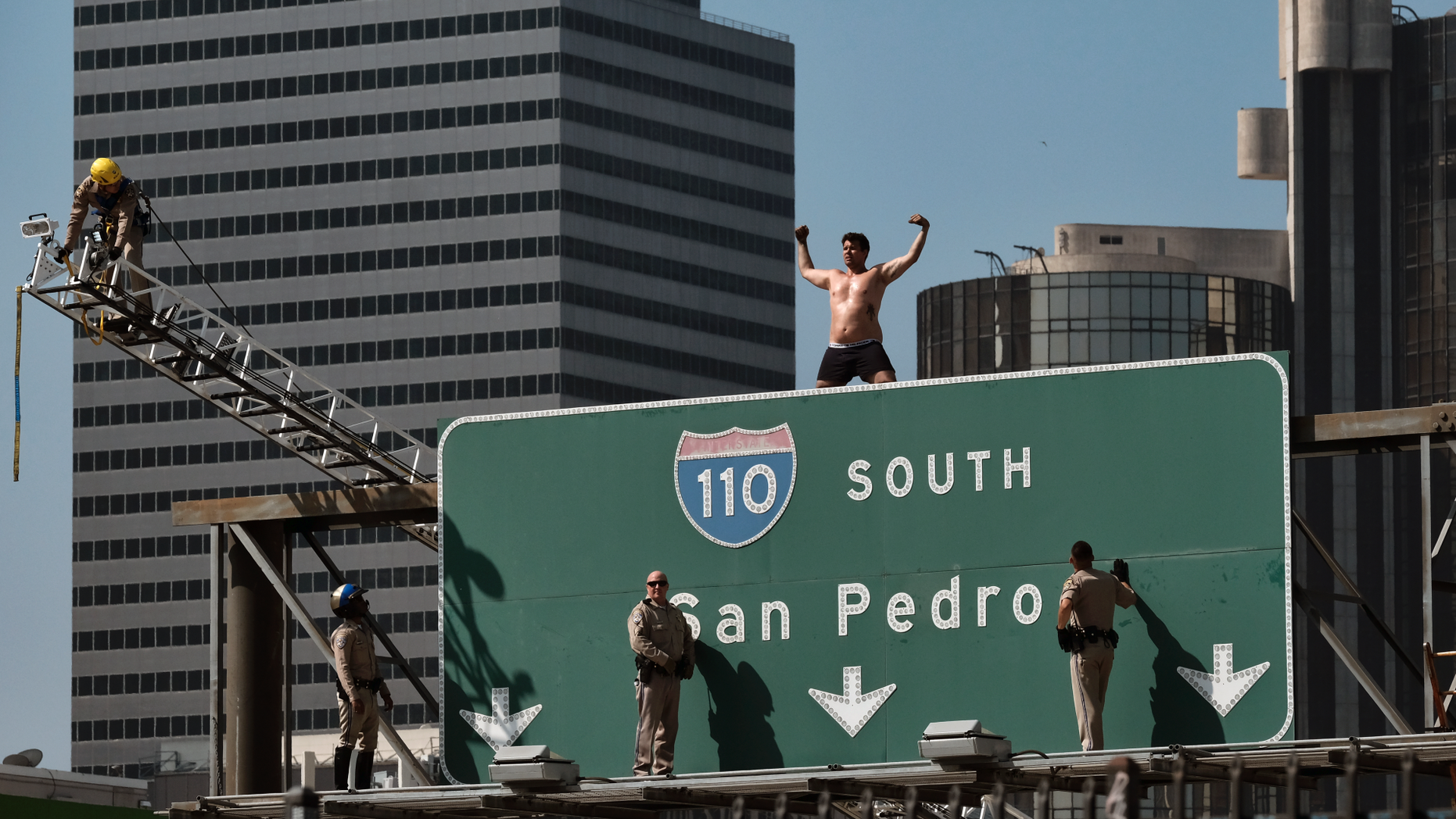 California Highway Patrol officers try to coax a man off a freeway sign in downtown Los Angeles.