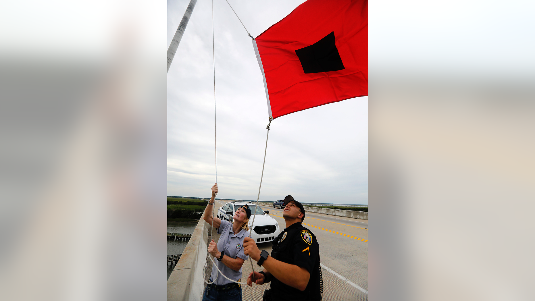 Isle of Palms Fire Chief Ann Graham, at left, and Isle of Palms police officer Thomas Molino III raise a tropical storm warning flag over the Isle of Palms Connector shortly after Charleston County, S.C., went under a tropical storm warning due to Hurricane Florence Thursday, Sept. 13, 2018, in Isle of Palms, S.C. (AP Photo/Mic Smith)