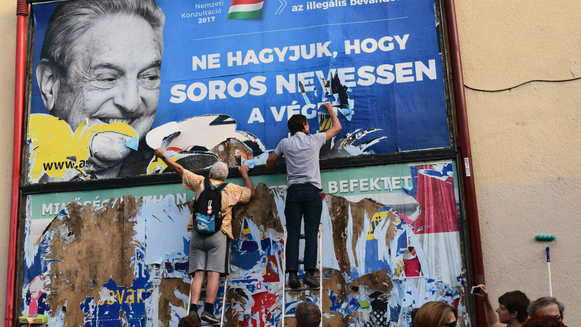 FILE -- In this Wednesday, July 12, 2017 photo activists of the Egyutt (Together) party tear down an ad by the Hungarian government against George Soros, in Budapest, Hungary. The Open Society Foundations, created by billionaire philanthropist George Soros, says it has filed applications before the European Court of Human Rights and Hungary's Constitutional Court about recent laws in Hungary targeting civic groups working with refugees and asylum-seekers. (AP Photo/Pablo Gorondi, file)