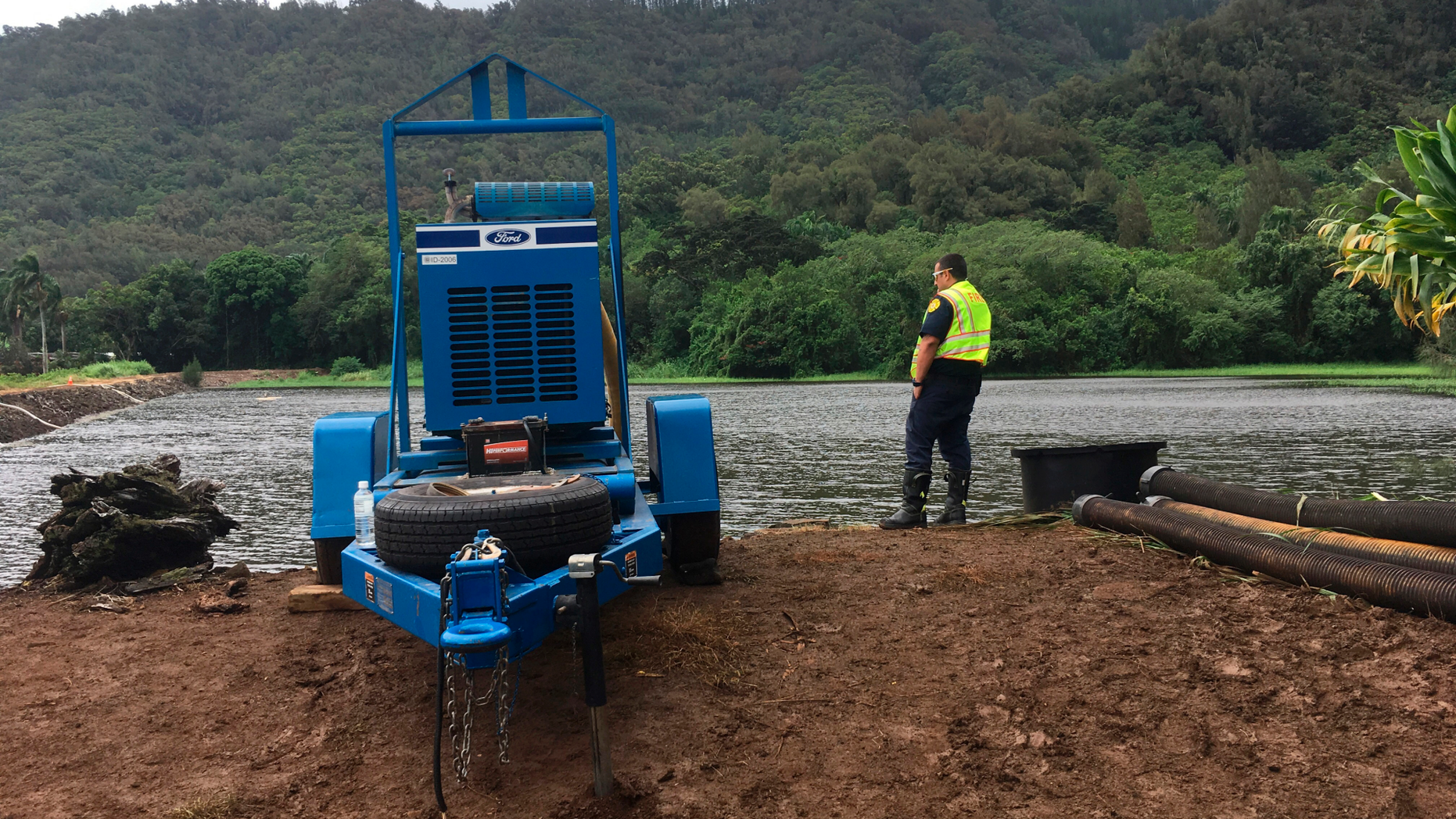 A fire official watches as water is pumped from a reservoir where a dam came close to overflowing in Honolulu on Thursday, Sept. 13, 2018. Honolulu officials say they may need to evacuate 10,000 people from a residential neighborhood if water in the reservoir continues to rise after heavy rains from a tropical storm. (AP Photo/Caleb Jones)