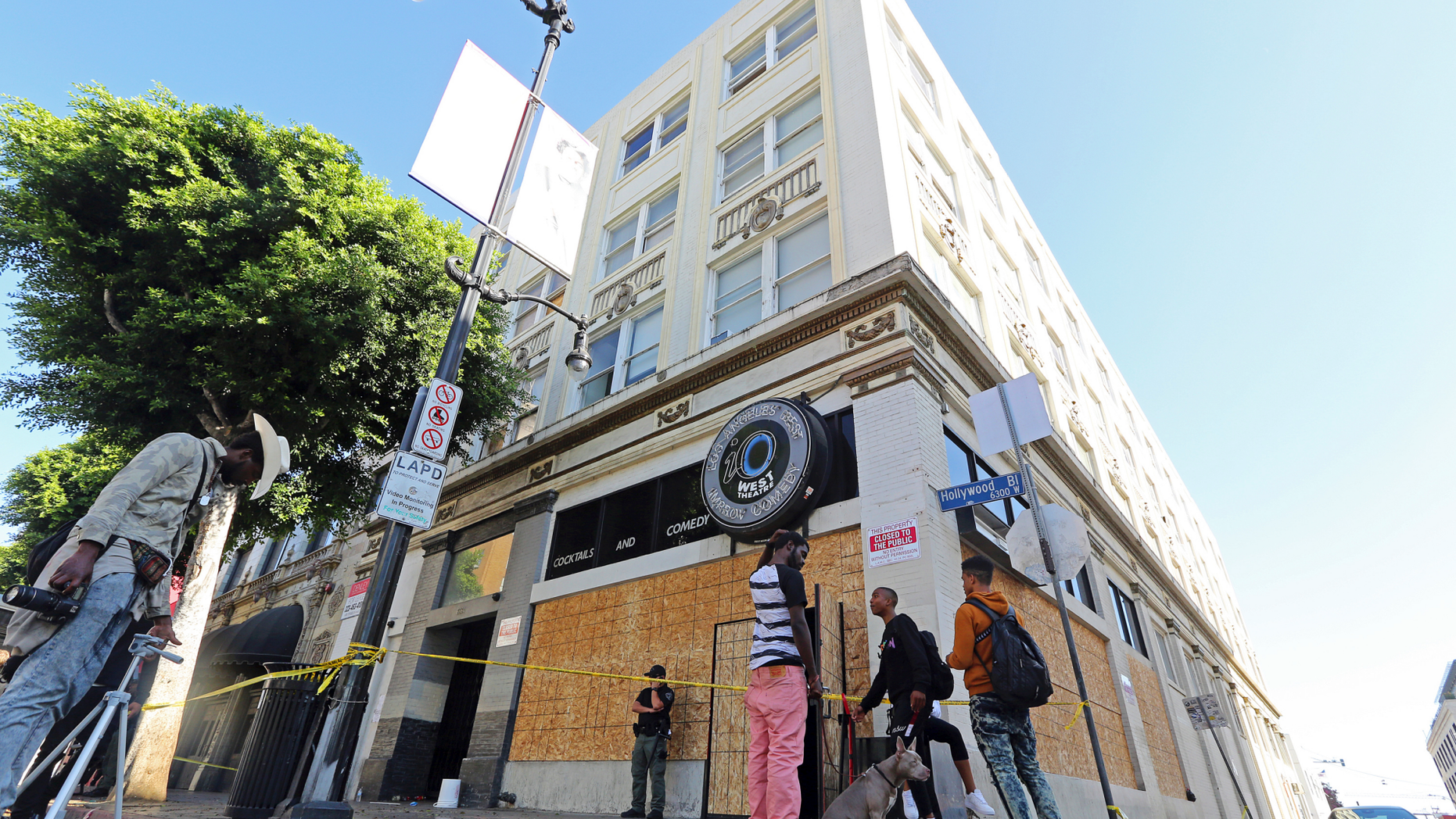 People who may have been occupants and others stand around a four-story vacant commercial building in Los Angeles' Hollywood district that was raided early in the morning of Wednesday, Sept. 12, 2018. Los Angeles police say more than 60 adults and at least four juveniles were detained during the raid where some people had been squatting. A search warrant was served before dawn on Hollywood Boulevard and officers went through the building, room by room, over several hours. Two firearms — a shotgun and a rifle— and drugs were seized, officials said. (AP Photo/Reed Saxon)