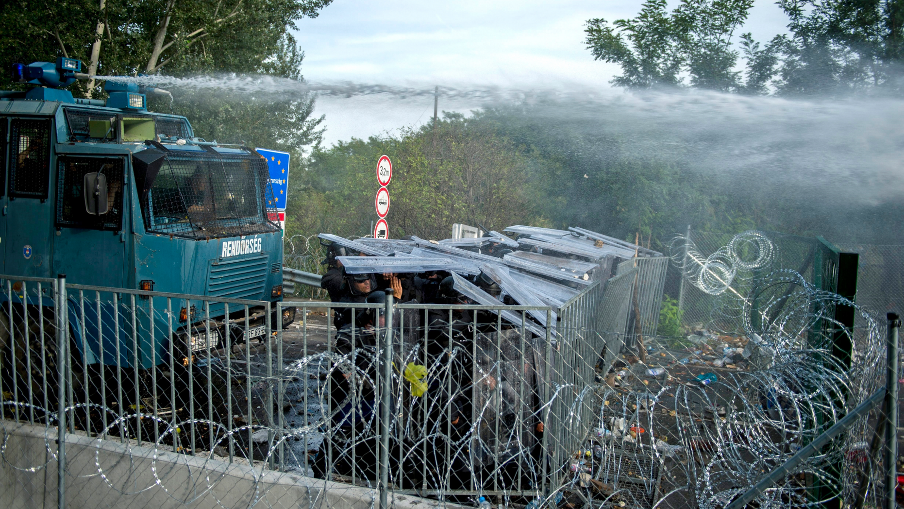 FILE - In this Sept. 16, 2015 file photo Hungarian police use water canons against refugees at the "Horgos 2" border crossing into Hungary, near Horgos, Serbia. A Hungarian appeals court on Thursday lowered to five years from seven the prison sentence of a Syrian man convicted of entering Hungary illegally and of complicity in throwing rocks at police during a 2015 border riot. The case stems from rioting at the Hungary-Serbia border on Sept. 16, 2015, when dozens of police officers, migrants and some journalists were injured in clashes a day after Hungary closed the frontier, stranding hundreds of migrants. (Tamas Soki/MTI via AP, file)