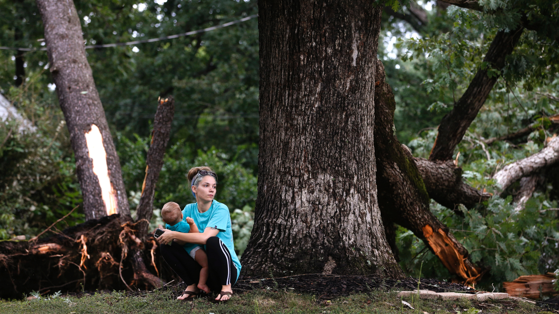 Sierra Price and son, Ryland Ross, 10 months, wait outside their home at Julian and Glendale Streets as work begins on cleanup in the area near Richmond,Virginia on Tuesday, Sept. 18, 2018, the day after Florence-spawned tornadoes caused damage and claimed one life in the area.( Joe Mahoney/Richmond Times-Dispatch via AP)