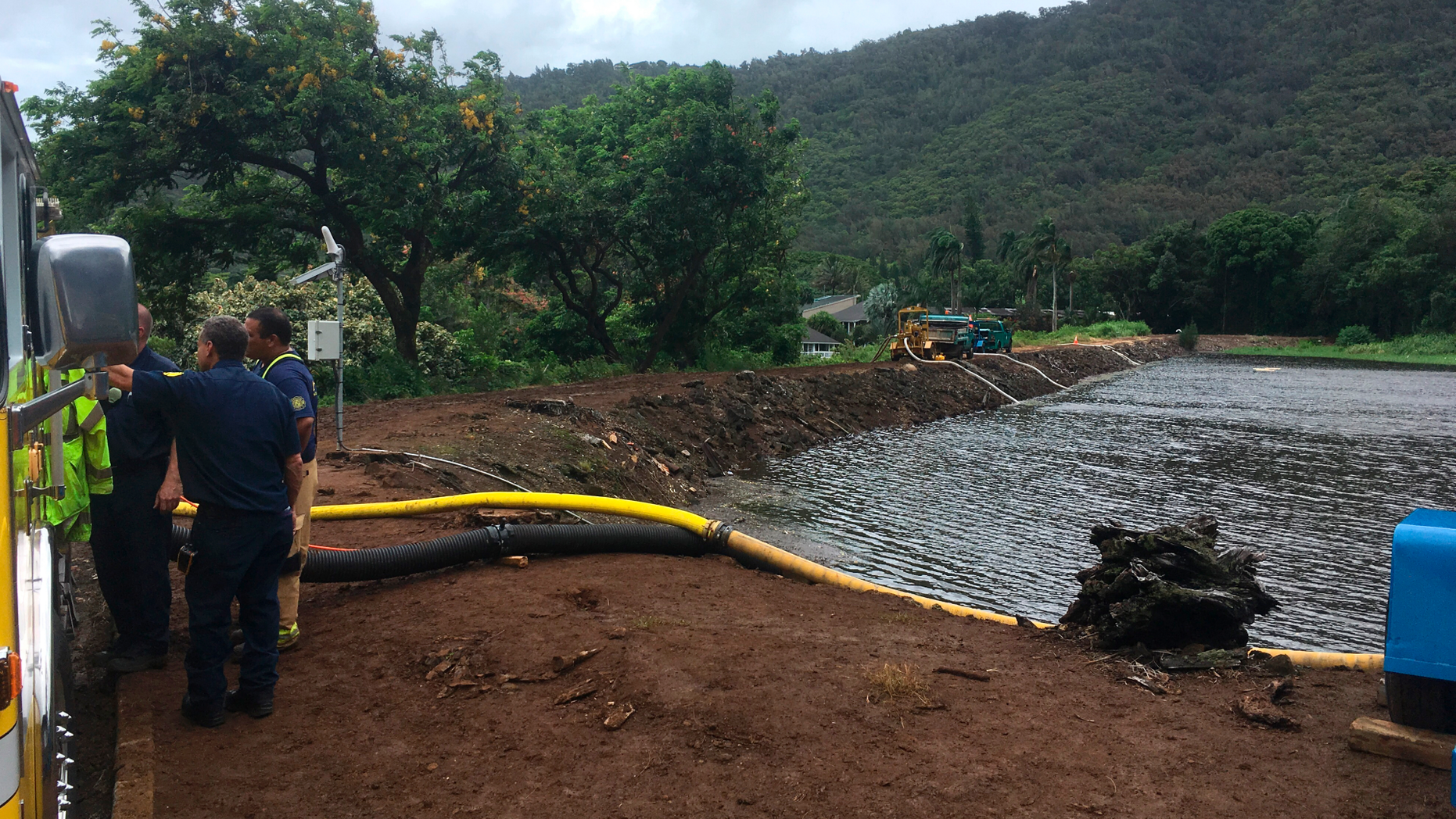 Officials pump water from a reservoir where a dam came close to overflowing in Honolulu on Thursday, Sept. 13, 2018. Honolulu officials say they may need to evacuate 10,000 people from a residential neighborhood if water in the reservoir continues to rise after heavy rains from a tropical storm. (AP Photo/Caleb Jones)