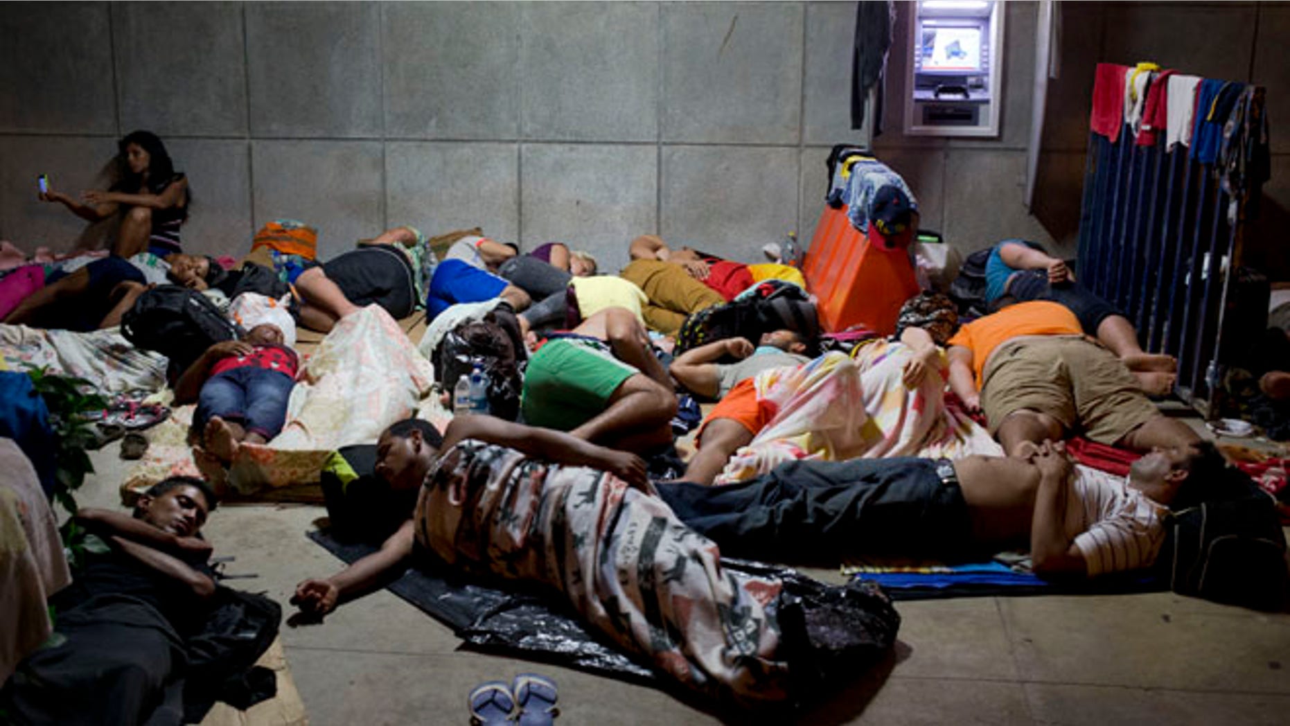 In this Nov. 21, 2015 file photo, a Cuban woman migrant uses her cell phone while other Cubans sleep, outside of the border control building in Penas Blancas, Costa Rica. (AP Photo/Esteban Felix, File)