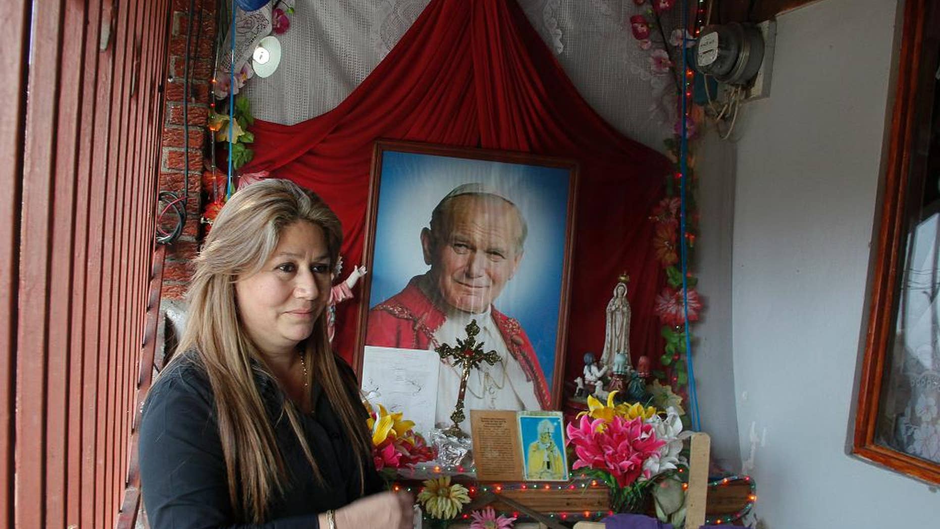 FILE - In this July 5, 2013 file photo, Floribeth Mora stands by her shrine to Pope John Paul II inside the entrance to her home in La Union de Cartago, Costa Rica. Mora, her doctors and the Catholic Church say her aneurysm disappeared in May of 2011 in a miracle that cleared the way for the late pope to be declared a saint. Mora will attend the ceremony at the Vatican on April 27, 2014 as a guest of honor. (AP Photo/Enrique Martinez, File)