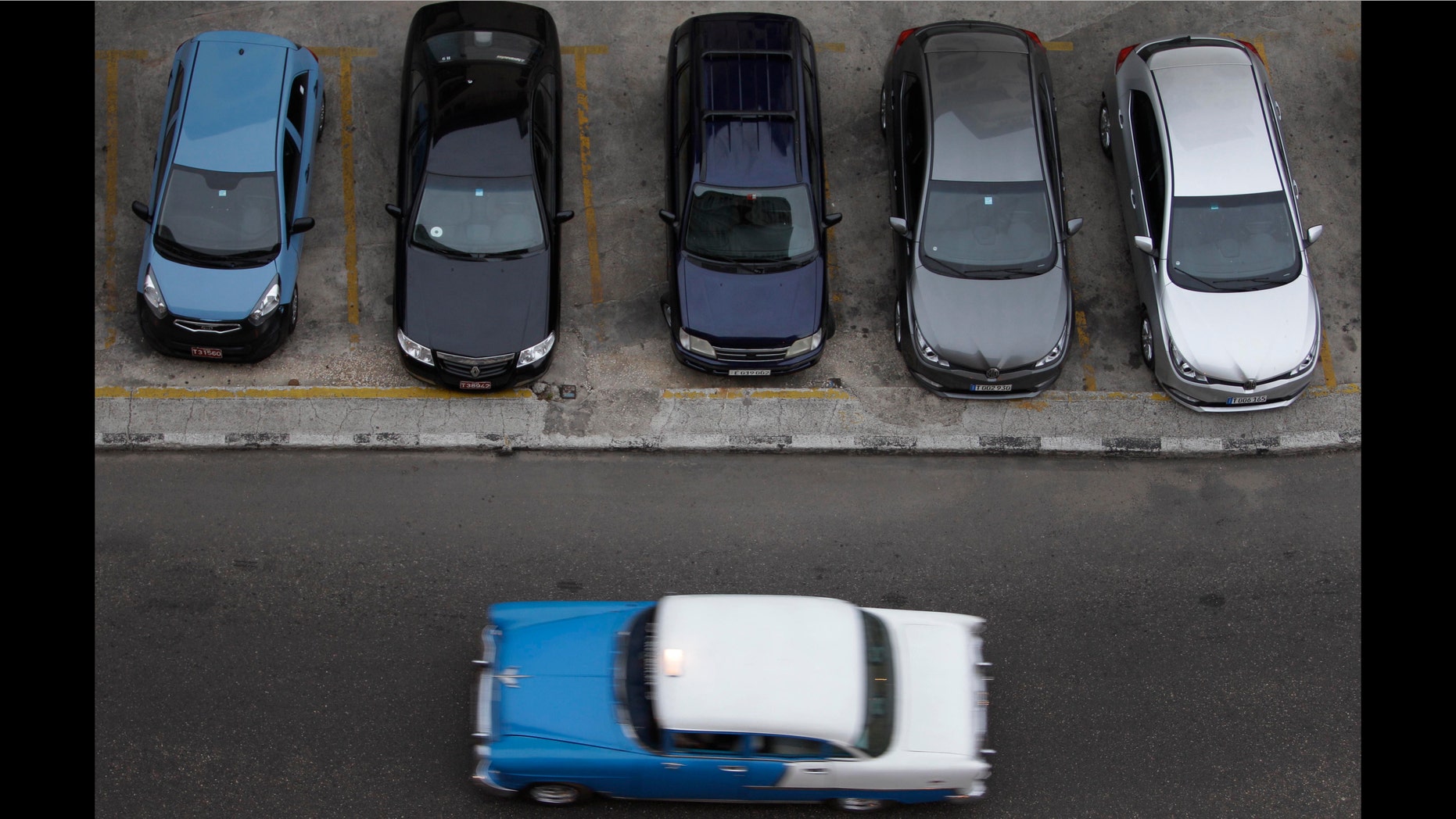 A vintage automobile drives by a parking lot of modern vehicles in Havana, Cuba, Thursday, Dec. 19, 2013. According to official media the government is opening the automobile market by eliminating the special permit that strictly limited the number of people allowed to buy vehicles from the state. (AP Photo/Franklin Reyes)