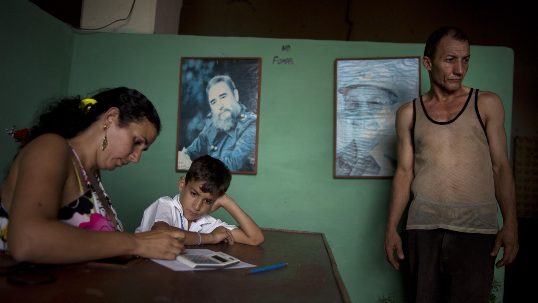 A worker, right, leaves the tobacco factory as a child waits for his mother to finish at a warehouse in the western province of Pinar del Rio, Cuba, Tuesday, Feb. 25, 2014. Pictures of Cuba's Fidel Castro and Raul Castro hang on the wall. Cigar enthusiasts from around the world come to Cuba during the annual Cigar Festival to visit tobacco farms and factories and savor new cigar brands. (AP Photo/Ramon Espinosa)