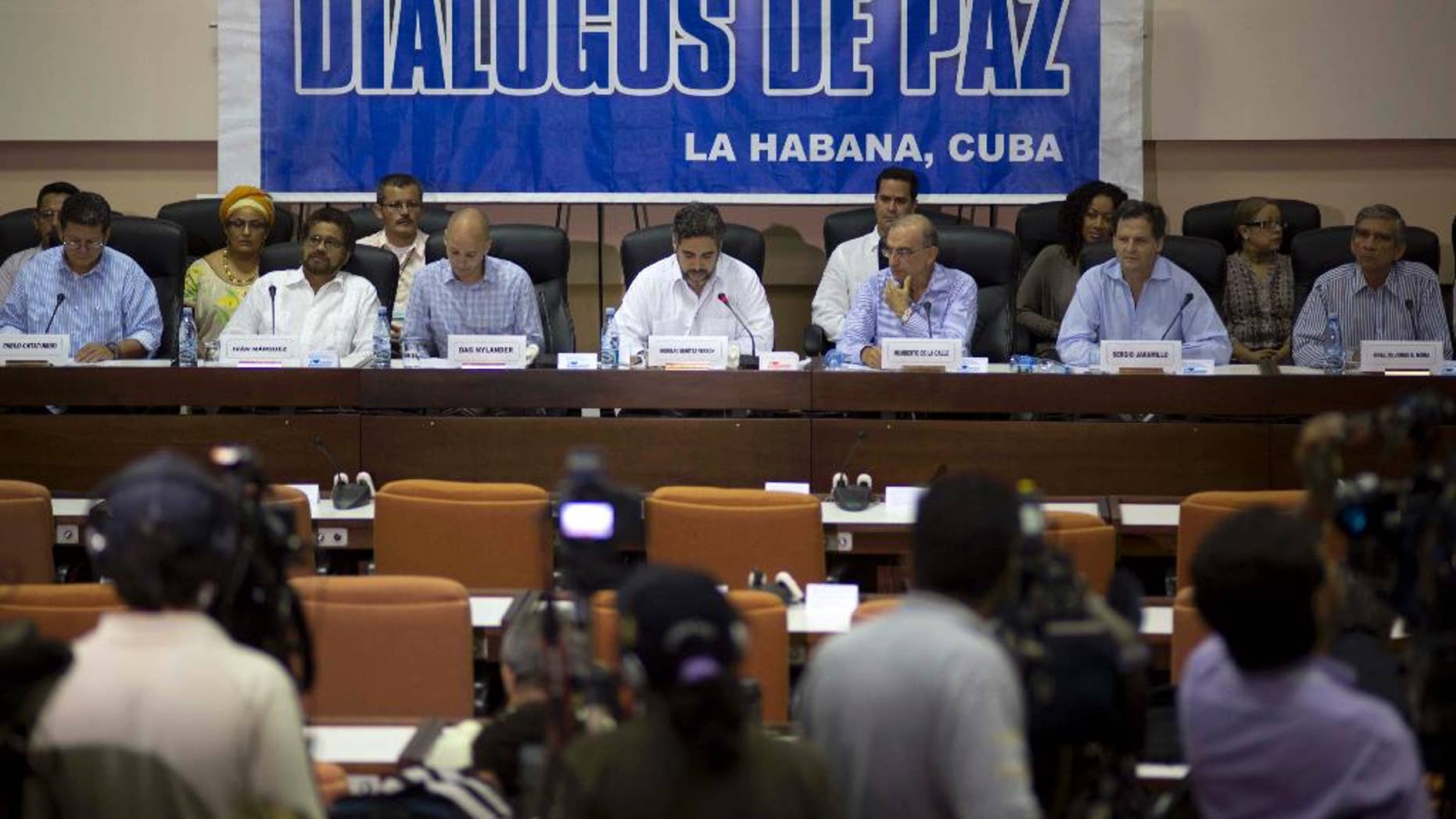FILE - In this May 16, 2014 file photo, negotiators from the Revolutionary Armed Forces of Colombia (FARC), left, and Colombia's government, right, give a press conference under a sign that reads in Spanish "Peace Talks" in Havana, Cuba. Colombia's government has rebuffed a unilateral truce declared on Wednesday, Dec. 18, 2014 by the country's largest rebel group, saying conditions demanded by the guerrillas’ are unacceptable until a peace deal is reached. Sitting at the table, from left, are chief of the western bloc of the FARC Pablo Catatumbo, FARC chief negotiator Ivan Marquez, Norwegian guarantor Dag Nylander, Cuban guarantor Rodolfo Benitez Verson, head of Colombia's government team Humberto de la Calle, government negotiator Sergio Jaramillo, and government negotiator Gen. Jorge Mora. (AP Photo/Ramon Espinosa, File)