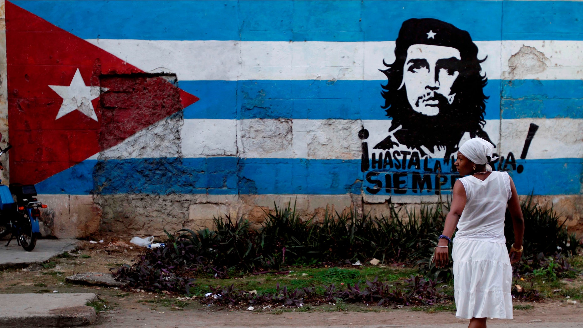 A santera looks back while crossing the street where a wall is covered with a mural of the Cuban flag and an image of Cuba's revolutionary hero Ernesto "Che" Guevara in Havana, Cuba, Friday Jan. 27, 2012. After economic reforms by President Raul Castro were endorsed by the communist congress in mid-2011, the Communist Party of Cuba (PCC) is preparing to hold a party conference this weekend. (AP Photo/Franklin Reyes)