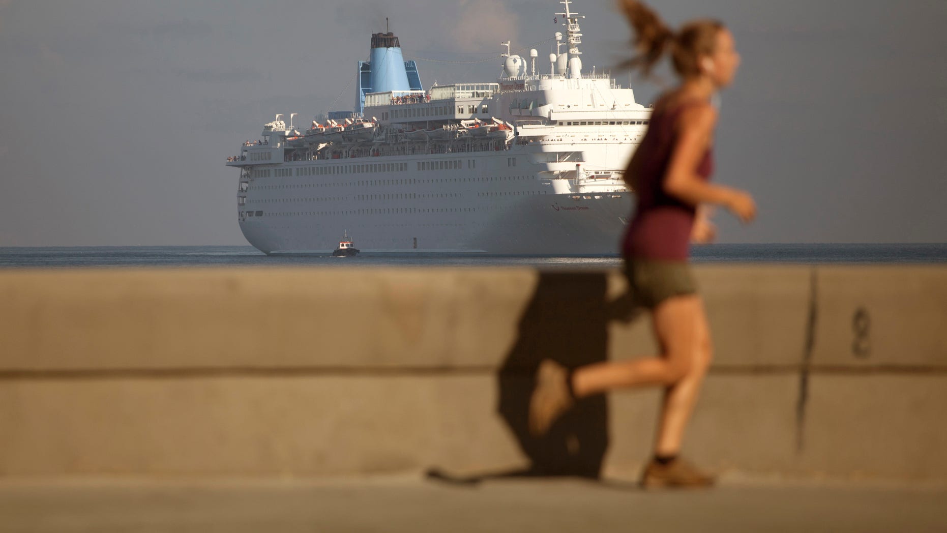 FILE - In this March 19, 2015, file photo, a woman jogs on the Malecon as the Thomson Dream cruise ship arrives in Havana bay. The Obama administration has approved on Tuesday, May 5, 2015, the first ferry service in decades between the United States and Cuba, potentially opening a new path for the hundreds of thousands of people and hundreds of millions of dollars in consumer goods that travel between Florida and Havana each year. (AP Photo/Desmond Boylan, File)