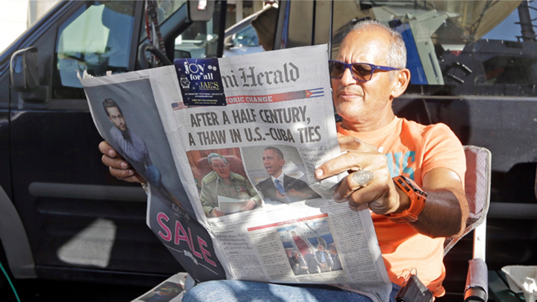 MSNBC photographer Tony Zumbado reads the Miami Herald in the Little Havana area of Miami, Thursday, Dec. 18, 2014, as news agencies from all over the world prepare to cover the reaction of the Cuban-Americans to the surprising move by President Barack Obama to restore the nation's ties with Cuba. The U.S. and Cuba will begin taking steps to restore full diplomatic relations, marking the most significant shift in U.S. policy toward the communist island in more than half a century. (AP Photo/Alan Diaz)