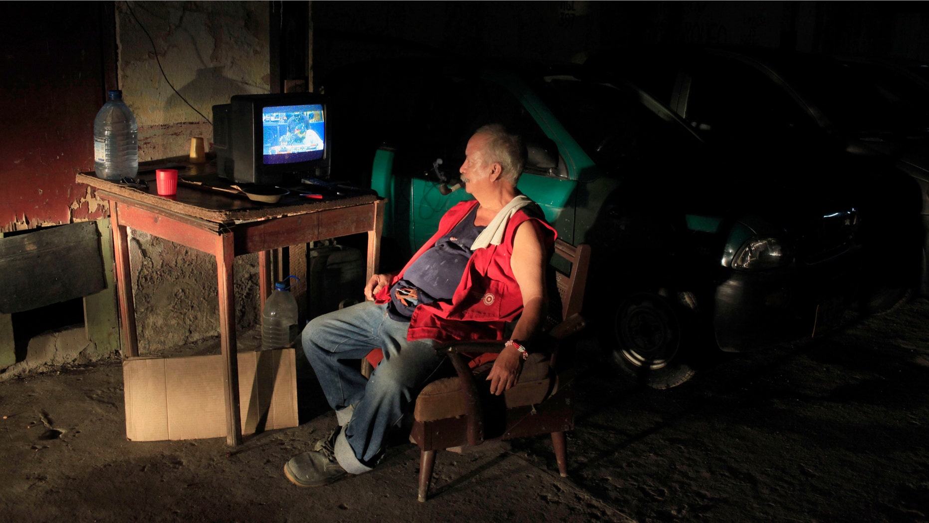 Andres Ortega, who works parking cars, is illuminated by an arriving car as he watches a baseball game between the Atlanta Braves and Washington Nationals that was played in May, on state television in Havana, Cuba, late Sunday, June 30, 2013. Cubans got a rare treat when state TV carried a Major League Baseball game for the first time in more than 50 years, but expressed disappointment when it turned out to be a nearly two-month old match-up without any of the defected Cuban stars whom islanders are most eager to follow. (AP Photo/Franklin Reyes)