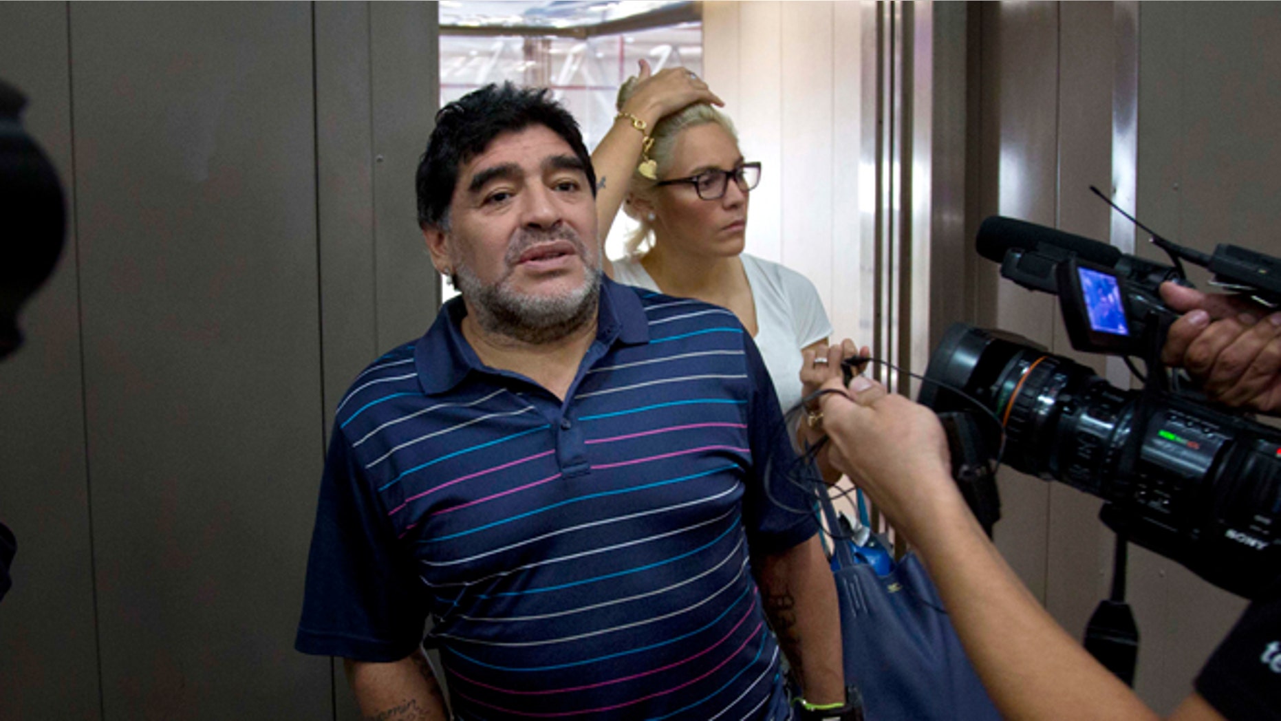 Argentina's soccer legend Diego Armando Maradona talks to journalists at the airport on his way to catch a departing plane in Havana, Cuba, Monday, Jan. 12, 2015. Behind is his girlfriend Rocio Oliva. Fidel Castro on Monday sent Maradona a letter written to quash rumors of the Cuban leader's death, state-run television network Telesur reported. It was the first reported word from Castro in nearly three months. The network showed photos of Maradona with the letter signed by Castro, 88. Telesur revealed nothing about the contents of the letter, but said it rebutted rumors he had died. (AP Photo/Ramon Espinosa)